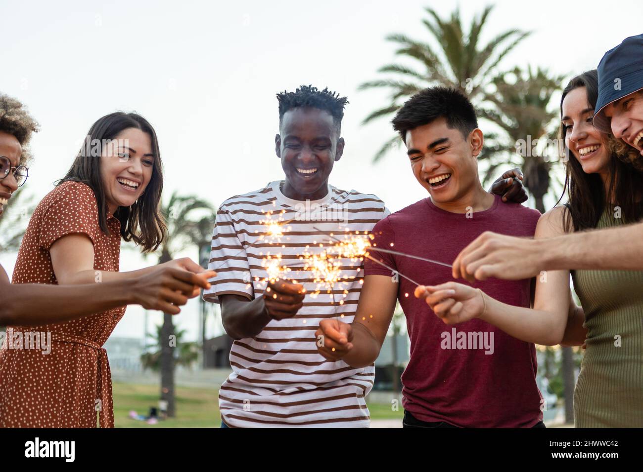Multiethnische glückliche junge Freunde, die Spaß am Halten haben, funkeln am Festivalabend Stockfoto