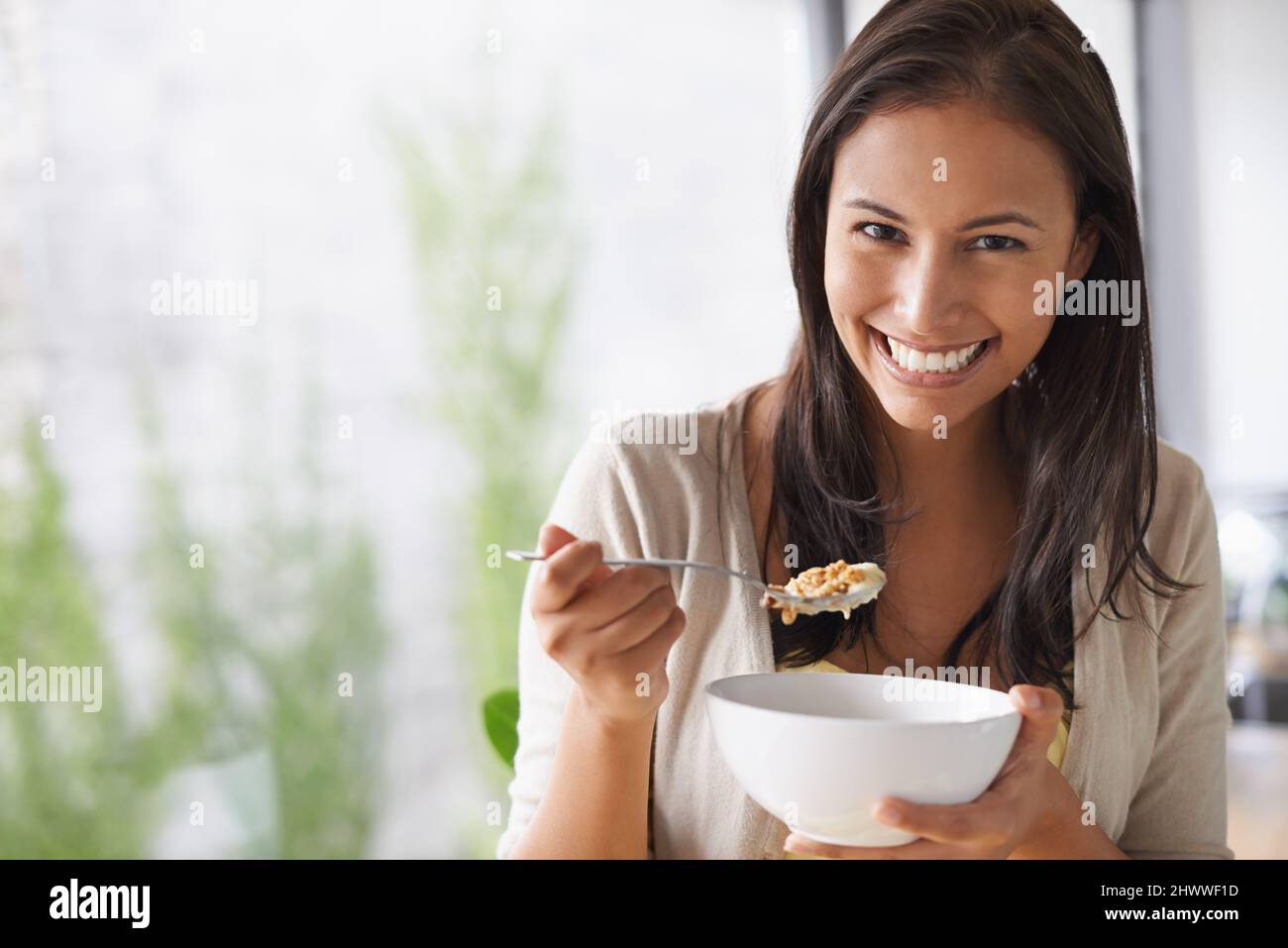 Sie liebt den frischen Geschmack ihrer Frühstücksflocken. Eine schöne junge Frau, die einen gesunden Salat genießt. Stockfoto