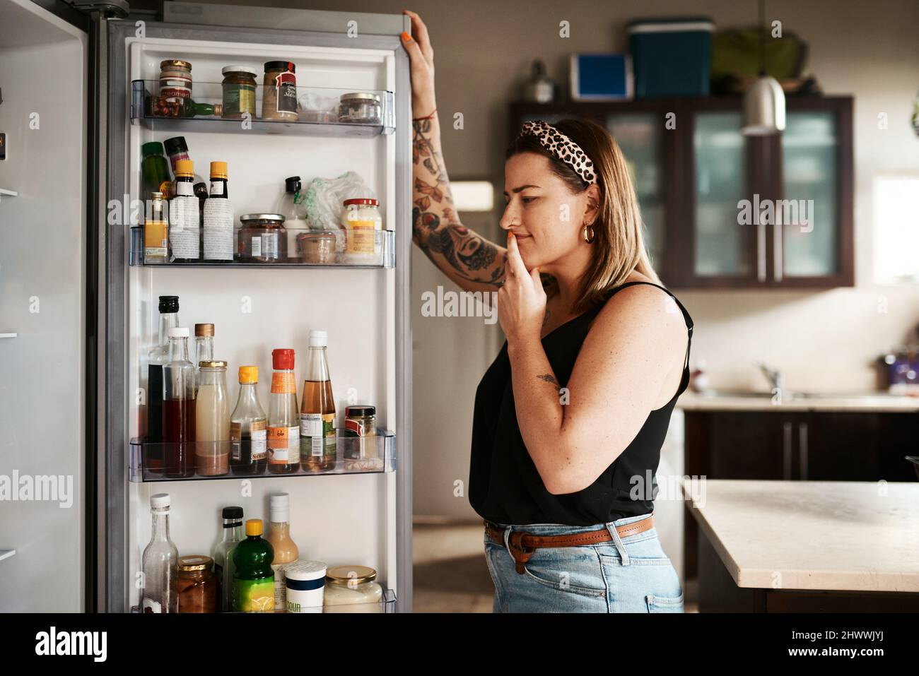 Hmm... was man zum Abendessen machen soll. Aufnahme einer jungen Frau, die zu Hause in einem Kühlschrank sucht. Stockfoto