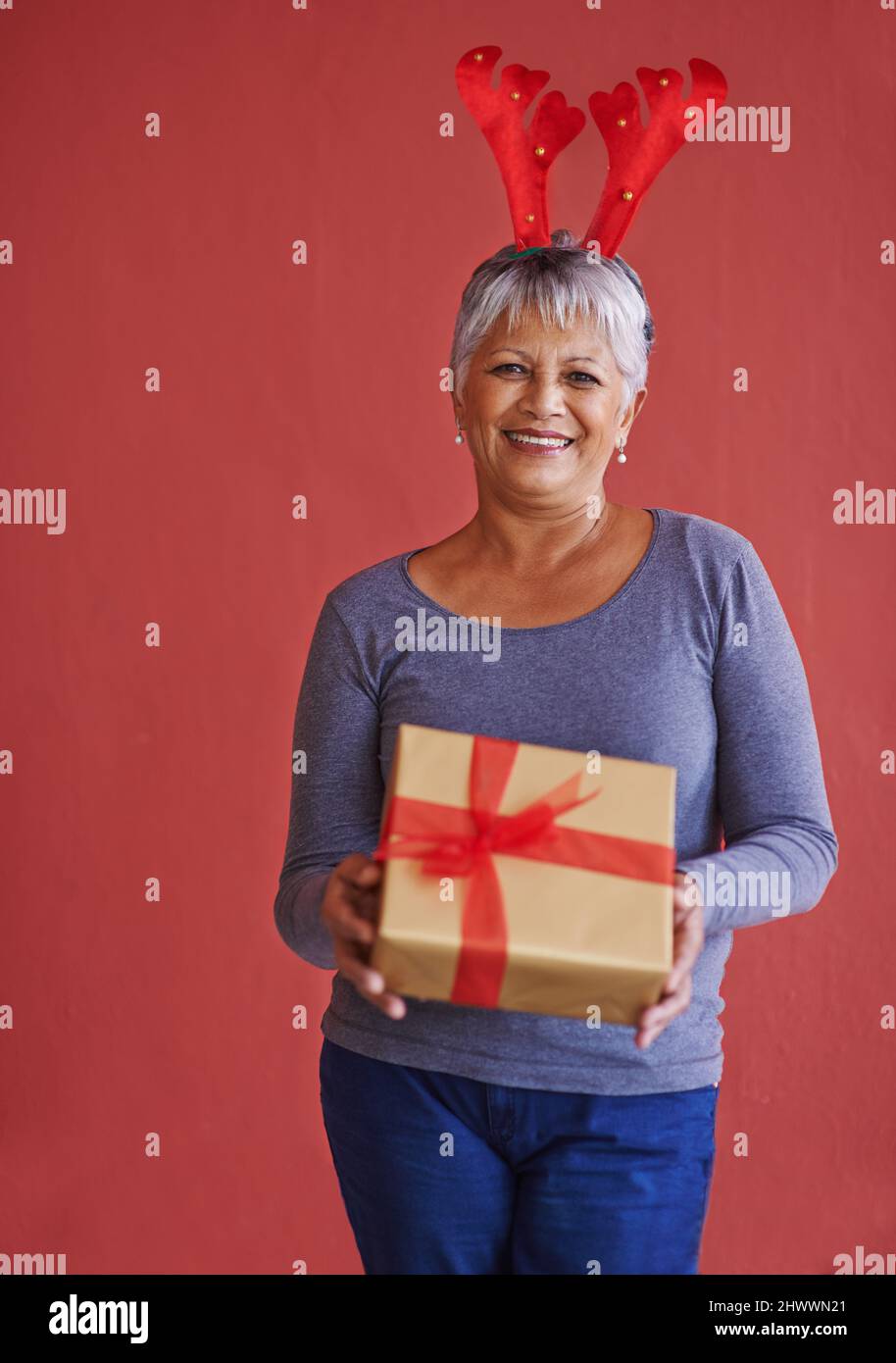 Hier ist etwas für Sie. Aufnahme einer reifen Frau mit einem Geschenk und festlichem Rentiergeweih. Stockfoto