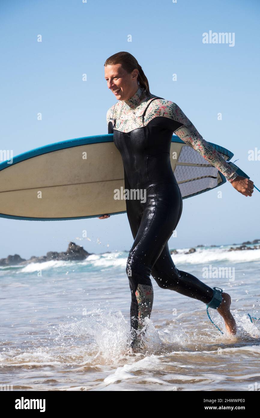 Glücklicher kaukasischer Surfer, der nach dem Wellenreiten aus dem Meer herauskam Stockfoto