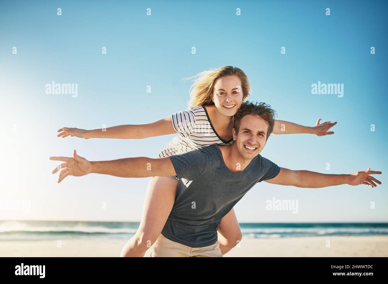 Liebe lässt uns lebendig fühlen. Aufnahme eines glücklichen jungen Paares, das eine Huckepack-Fahrt am Strand genießt. Stockfoto