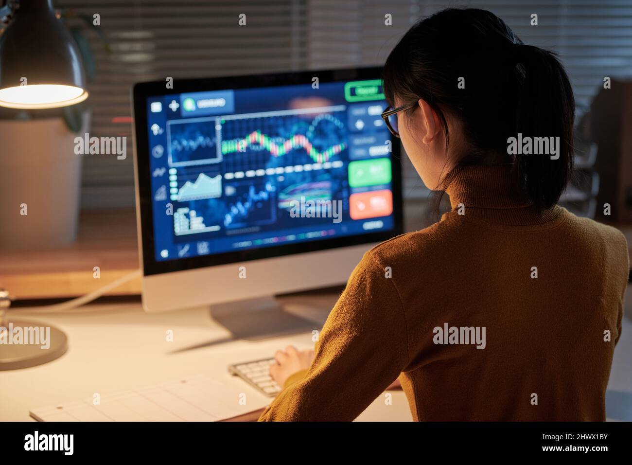 Rückansicht des jungen Computeringenieurs, der am Tisch vor dem Computermonitor sitzt und bis spät in die Nacht im Büro neue Software entwickelt Stockfoto