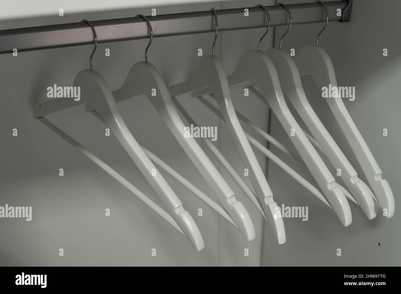 Nahaufnahme von weißen Kleiderbügeln. Kleidung auf einer Schiene im Kleiderschrank. Stockfoto