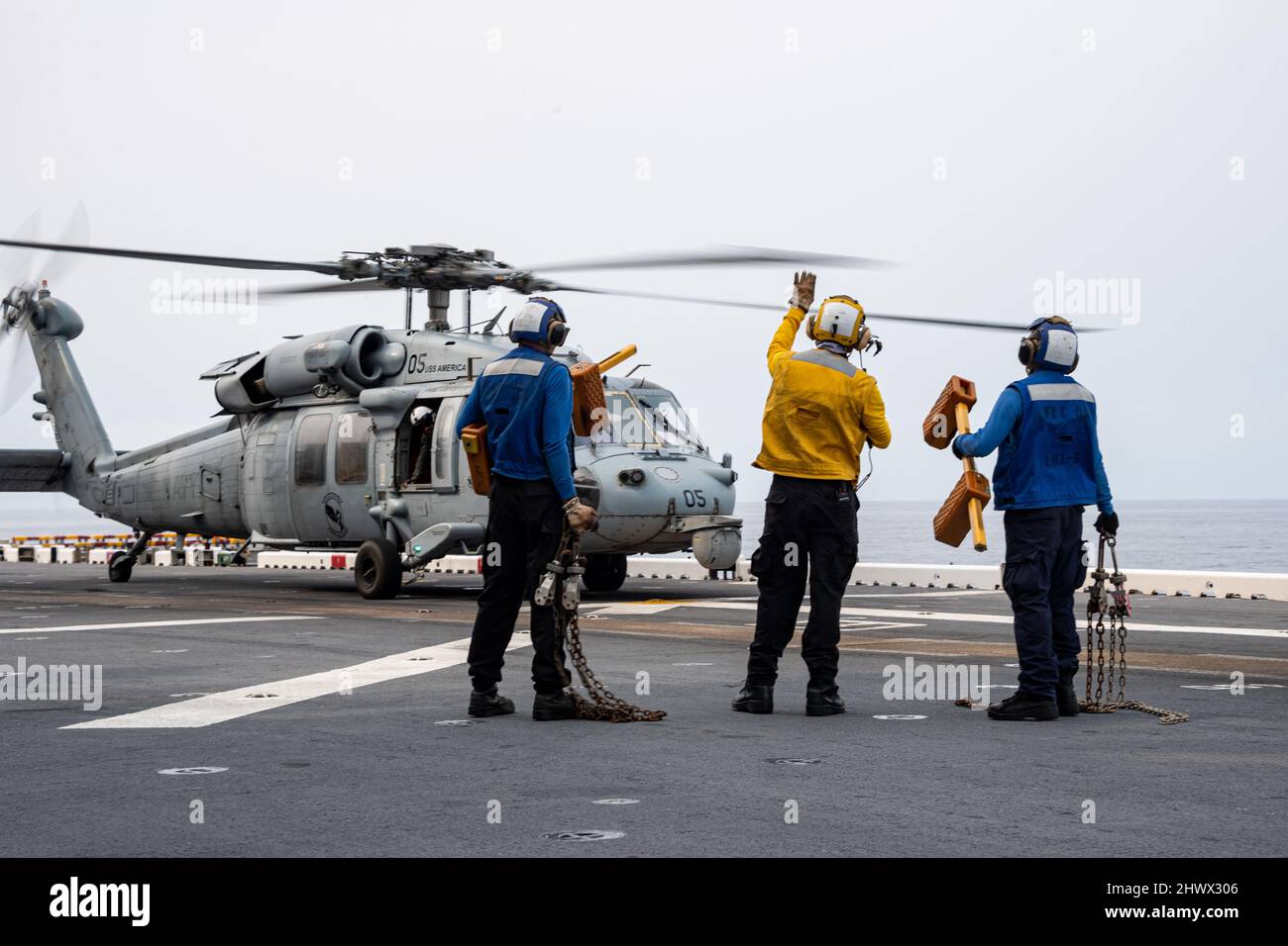 PHILIPPINISCHES MEER (März. 4, 2022) Seeleute, die dem nach vorne eingesetzten amphibischen Angriffsschiff USS America (LHA 6) zugewiesen wurden, signalisieren, dass Keile und Ketten von einem MH-60s Sea Hawk-Hubschrauber vom Helicopter Sea Combat Squadron (HSC) 25 auf dem Flugdeck des Schiffes entfernt wurden. Amerika, das führende Schiff der America Amphibious Ready Group, arbeitet zusammen mit der 31. Marine Expeditionary Unit im Verantwortungsbereich der US-Flotte für 7., um die Interoperabilität mit Verbündeten und Partnern zu verbessern und als einsatzbereite Einsatztruppe für den Frieden und die Stabilität in der Indo-Pazifik-Region zu dienen. (USA Navy Foto von Mas Stockfoto