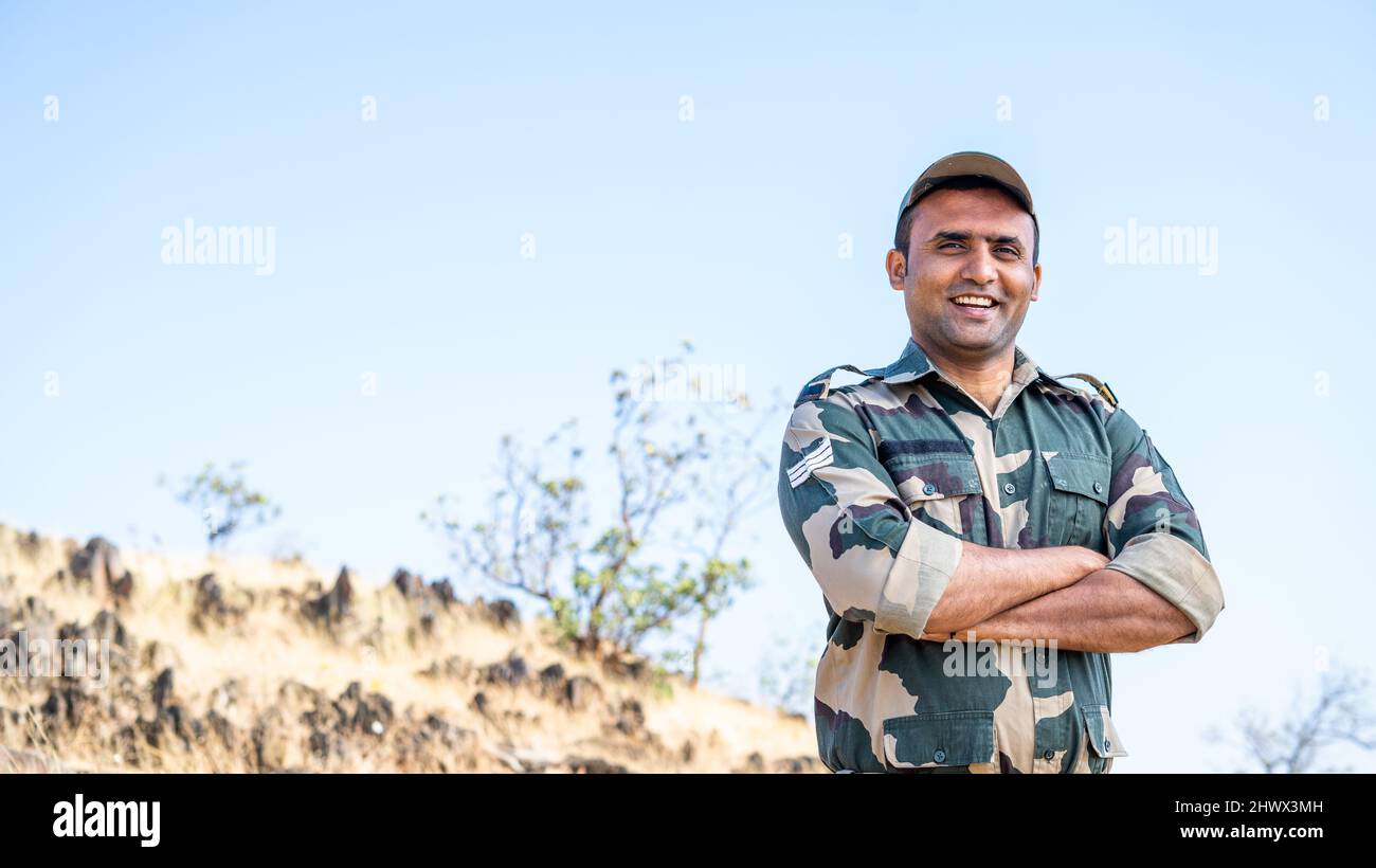 Selbstbewusster lächelnder indischer Soldat in Uniform, der mit gekreuzten Armen und Blick auf die Kamera steht - Konzept eines erfolgreichen, stolzen Soldaten und einer Besatzung. Stockfoto