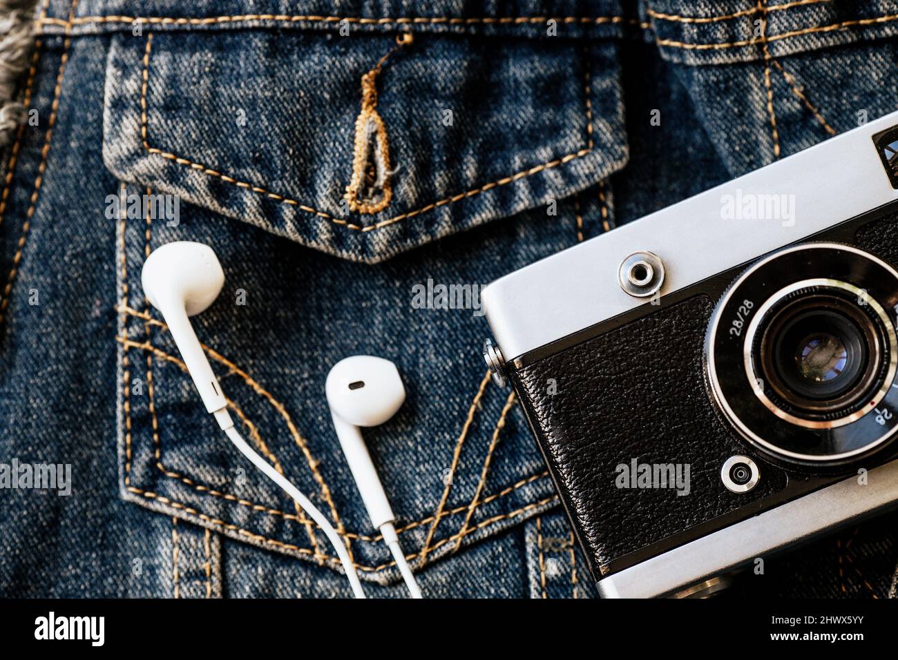 Filmkamera und weiße kabelgebundene Kopfhörer liegen vor dem Hintergrund von Denim. Modischer Hipster Hintergrund. Retro-Style. Tag des Fotografen. Draufsicht Stockfoto