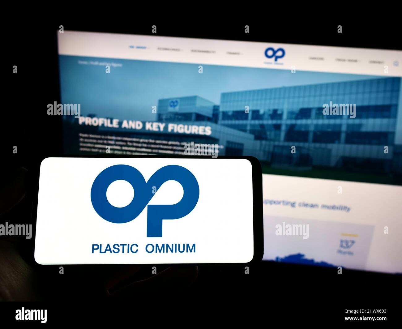 Person, die Mobiltelefon mit Logo der französischen Firma Compagnie Plastic Omnium SA auf dem Bildschirm vor der Business-Webseite hält. Konzentrieren Sie sich auf die Telefonanzeige. Stockfoto