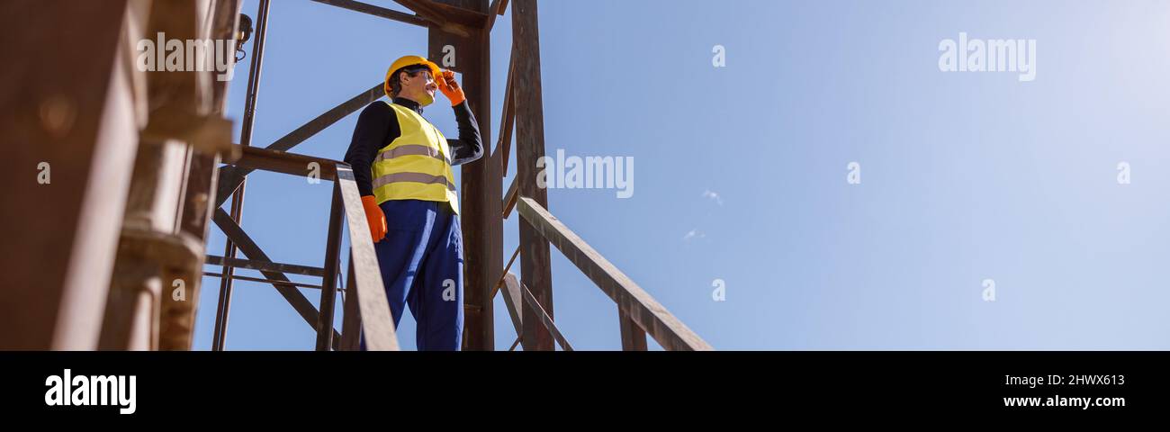 Männlicher Arbeiter, der auf einer Treppe unter blauem Himmel steht Stockfoto