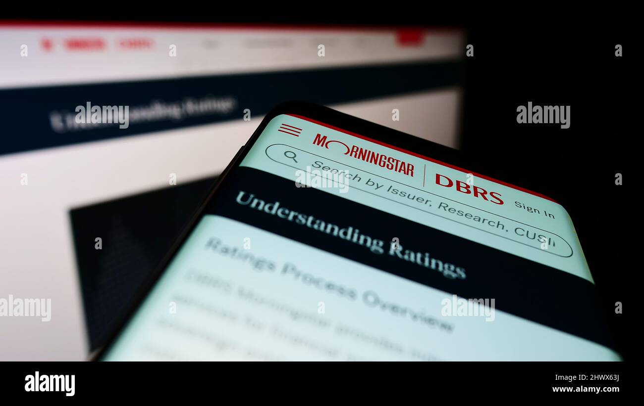 Smartphone mit Webseite des kanadischen Ratingunternehmens DBRS Morningstar auf dem Bildschirm vor dem Monitor. Konzentrieren Sie sich auf die obere linke Seite des Telefondisplays. Stockfoto