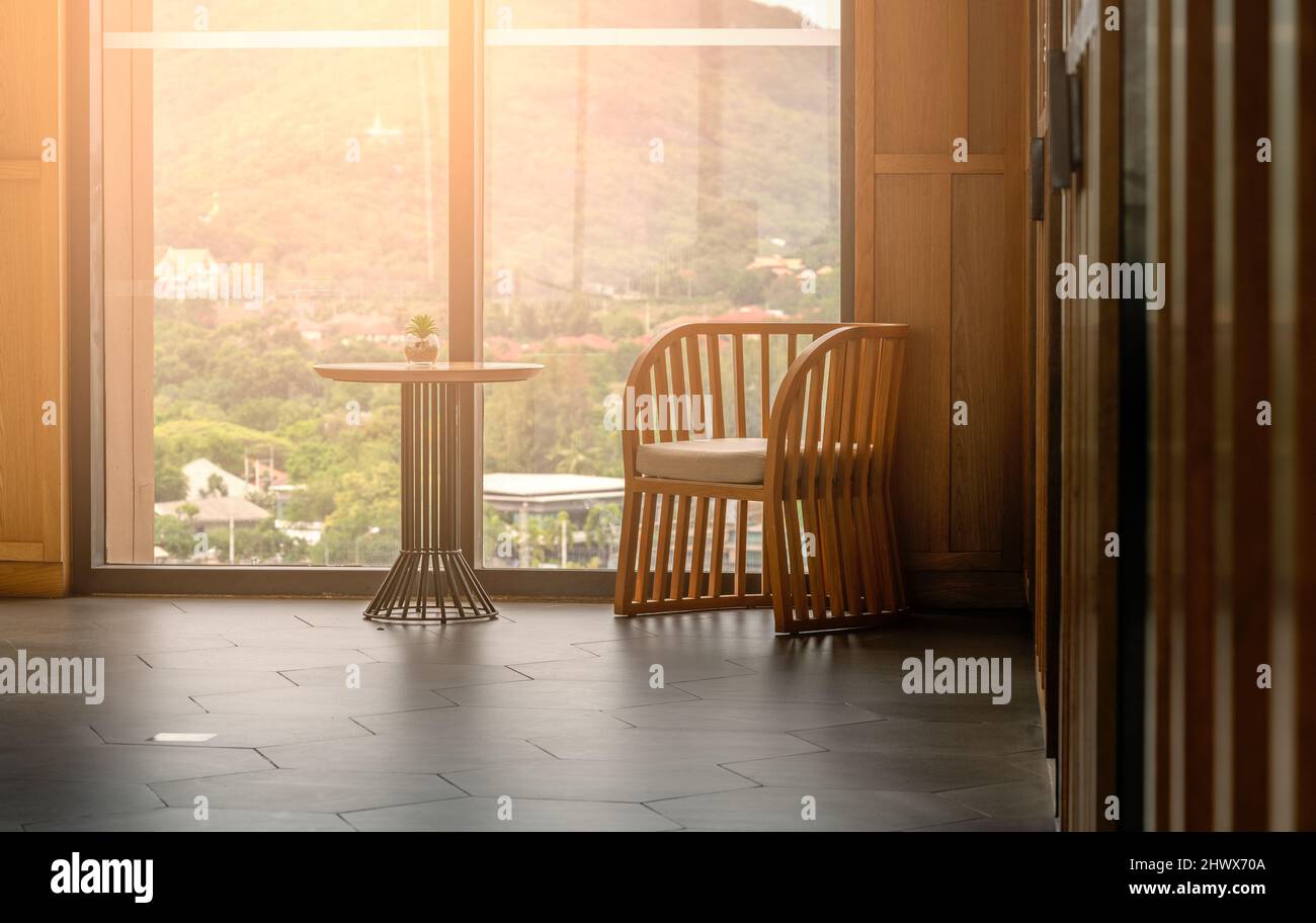 Man entspannt einen Stuhl und einen kleinen Schreibtisch mit einem kleinen Blumentopf aus Glas in einem Gebäude, Hintergrund einer großen Glasfensterwand und einer verschwommenen Berglandschaft Stockfoto