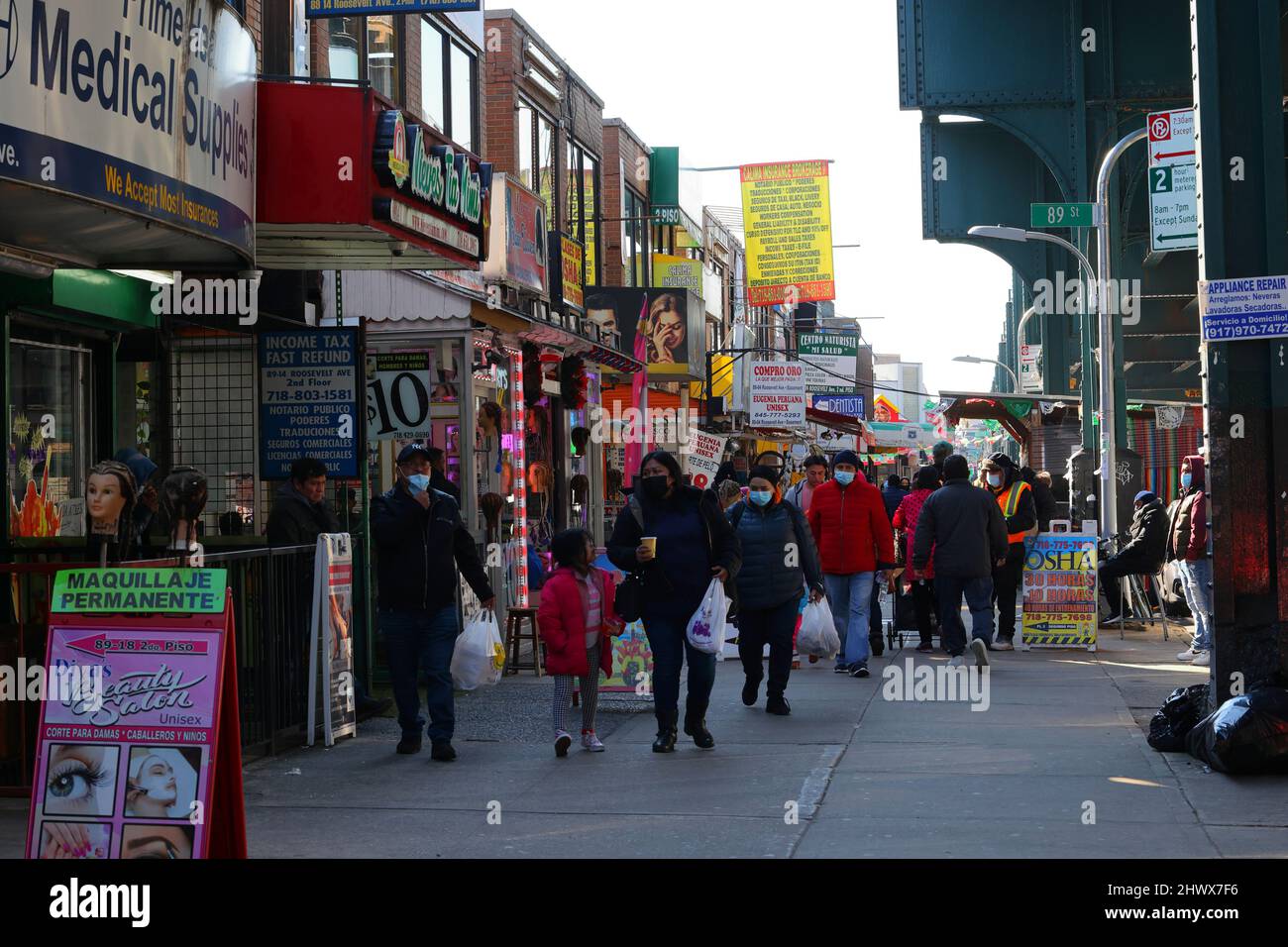 Menschen, die die Roosevelt Ave entlang laufen, umgeben von spanischen Schildern, die eine Vielzahl von Waren und Dienstleistungen anzeigen. Jackson Heights, Queens, New York. Stockfoto