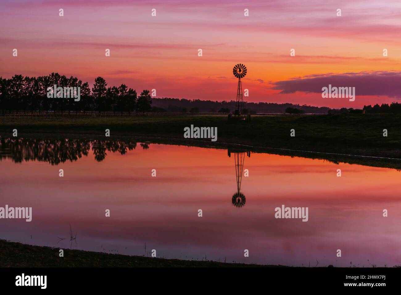 Alte Farm Windmühle in einem ländlichen Feld mit lebendigen Sonnenaufgangshimmel Stockfoto