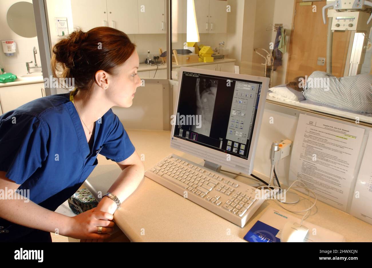 Der Radiologe sitzt im Kontrollraum, um den Röntgenscan durchzuführen. (MODELL FREIGEGEBEN) Stockfoto