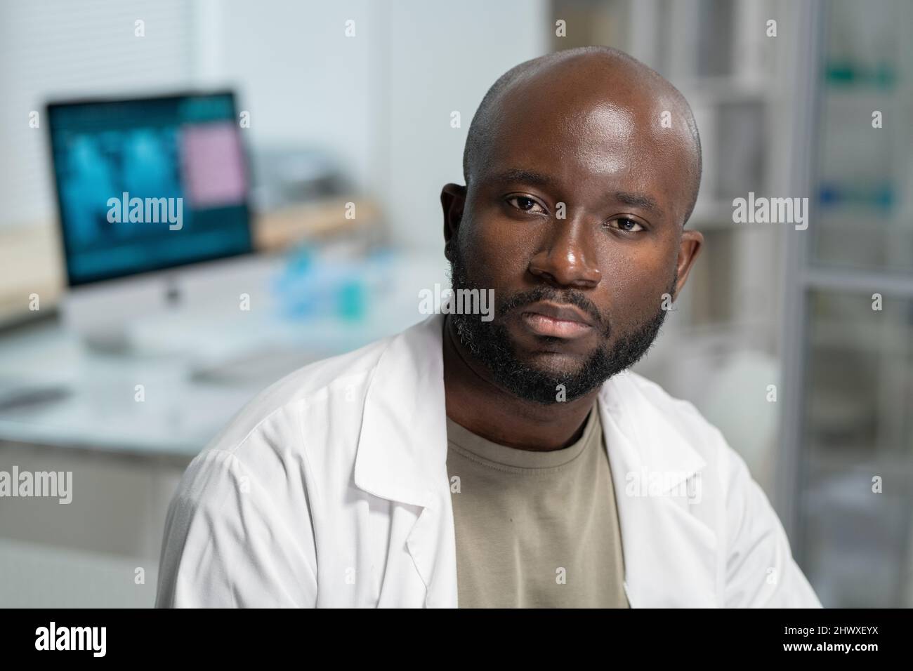 Porträt eines ernsthaften bärtigen Wissenschaftlers oder Chemikers im Labormantel, der während eines wissenschaftlichen Experiments im Labor vor der Kamera sitzt Stockfoto