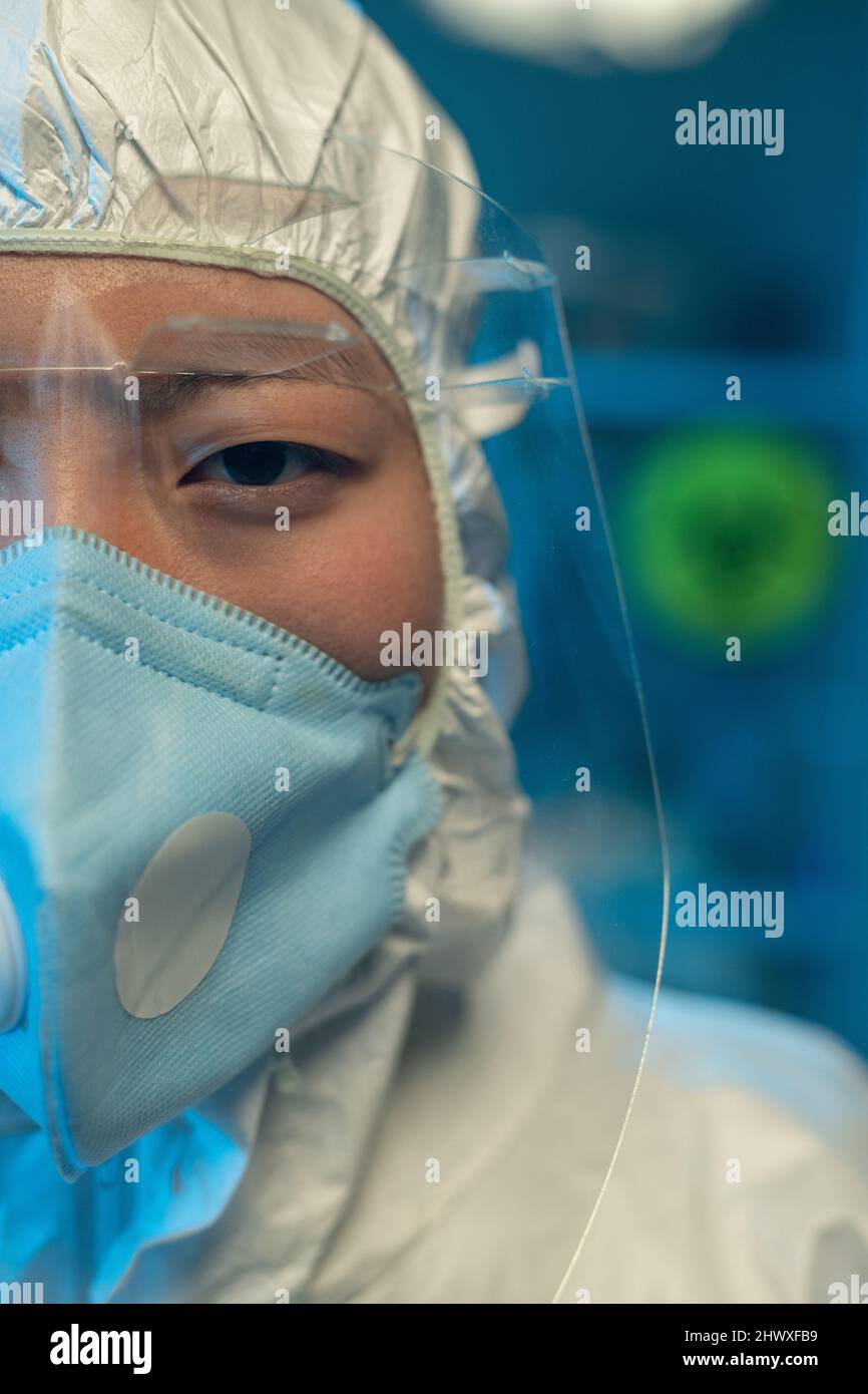 Die Hälfte des Gesichts einer jungen asiatischen Frau in Overalls, Atemschutzmaske und Schutzbrille, die vor der Kamera im Szintifielabor steht Stockfoto
