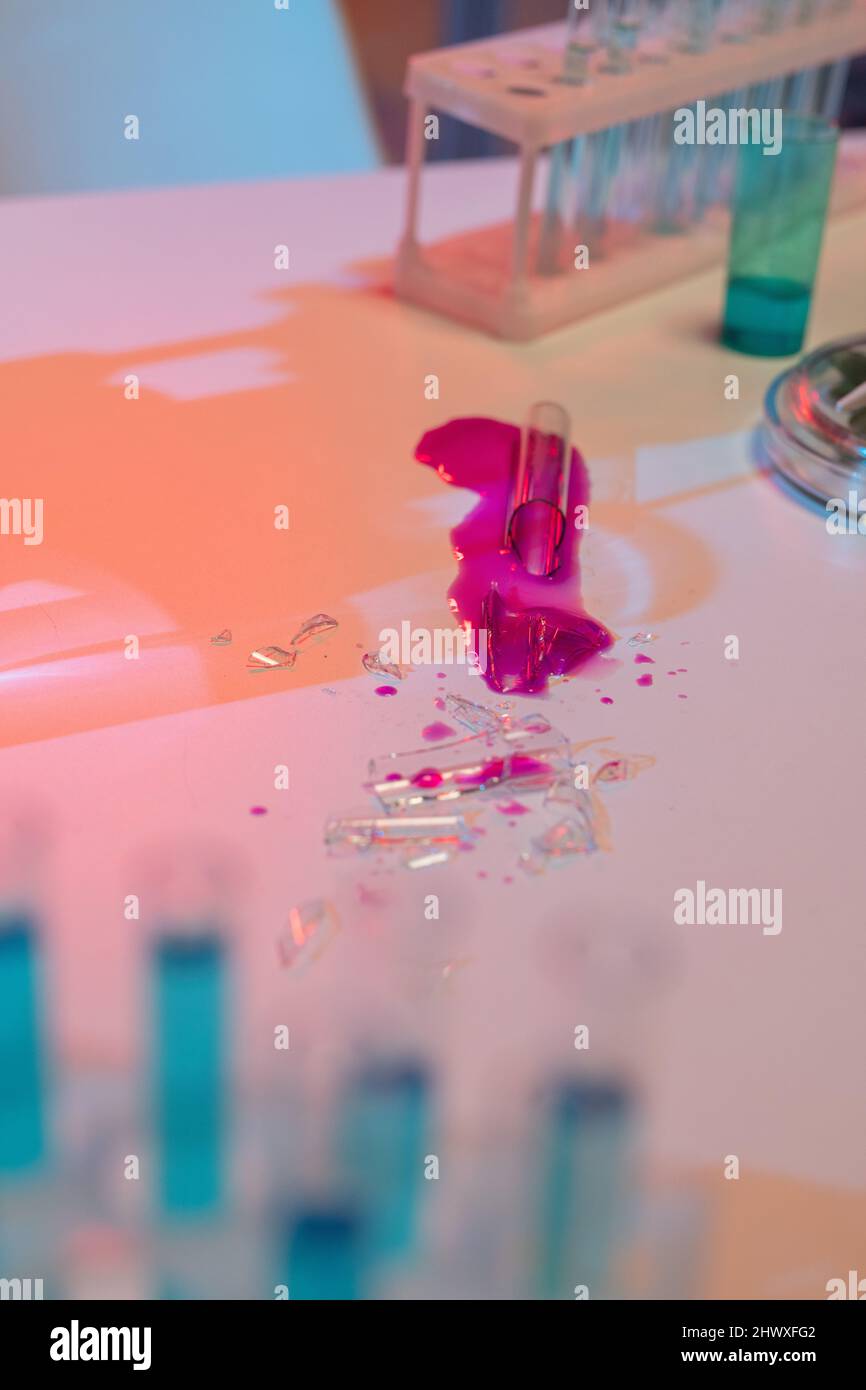 Die Scherben des zerbrochenen Glaskolben mit der gefährlichen chemischen Substanz der purpurnen Farbe auf dem Arbeitsplatz des Wissenschaftlers im modernen Labor Stockfoto