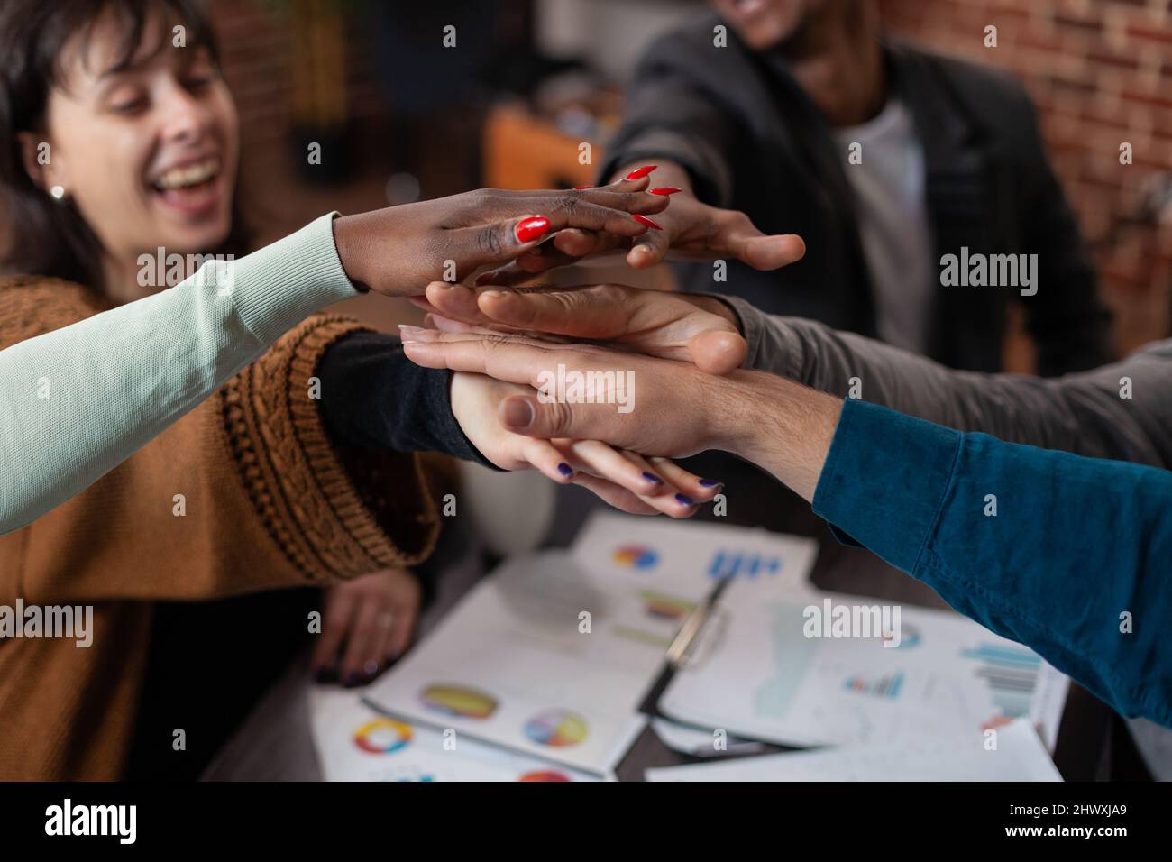 Nahaufnahme eines erfolgreichen, vielfältigen Teams, das lächelt und dabei Hand an Hand geht, um die Erfolge des Unternehmens während eines Geschäftstreffens bei der Arbeit im Startup Office zu feiern. Multiethnische Geschäftsleute genießen zusammen Stockfoto