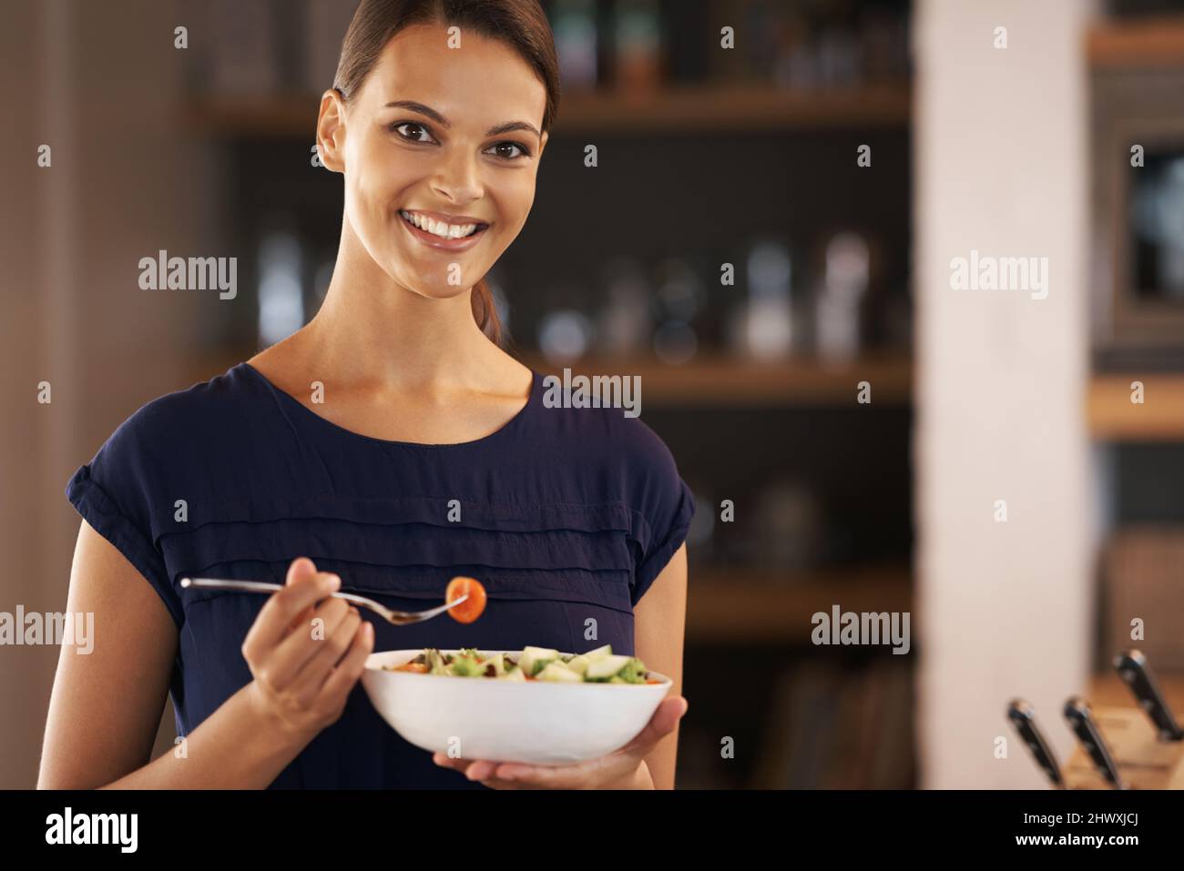 Was ich esse, ist wer ich bin. Eine schöne junge Frau, die zu Hause eine Schüssel Salat isst. Stockfoto