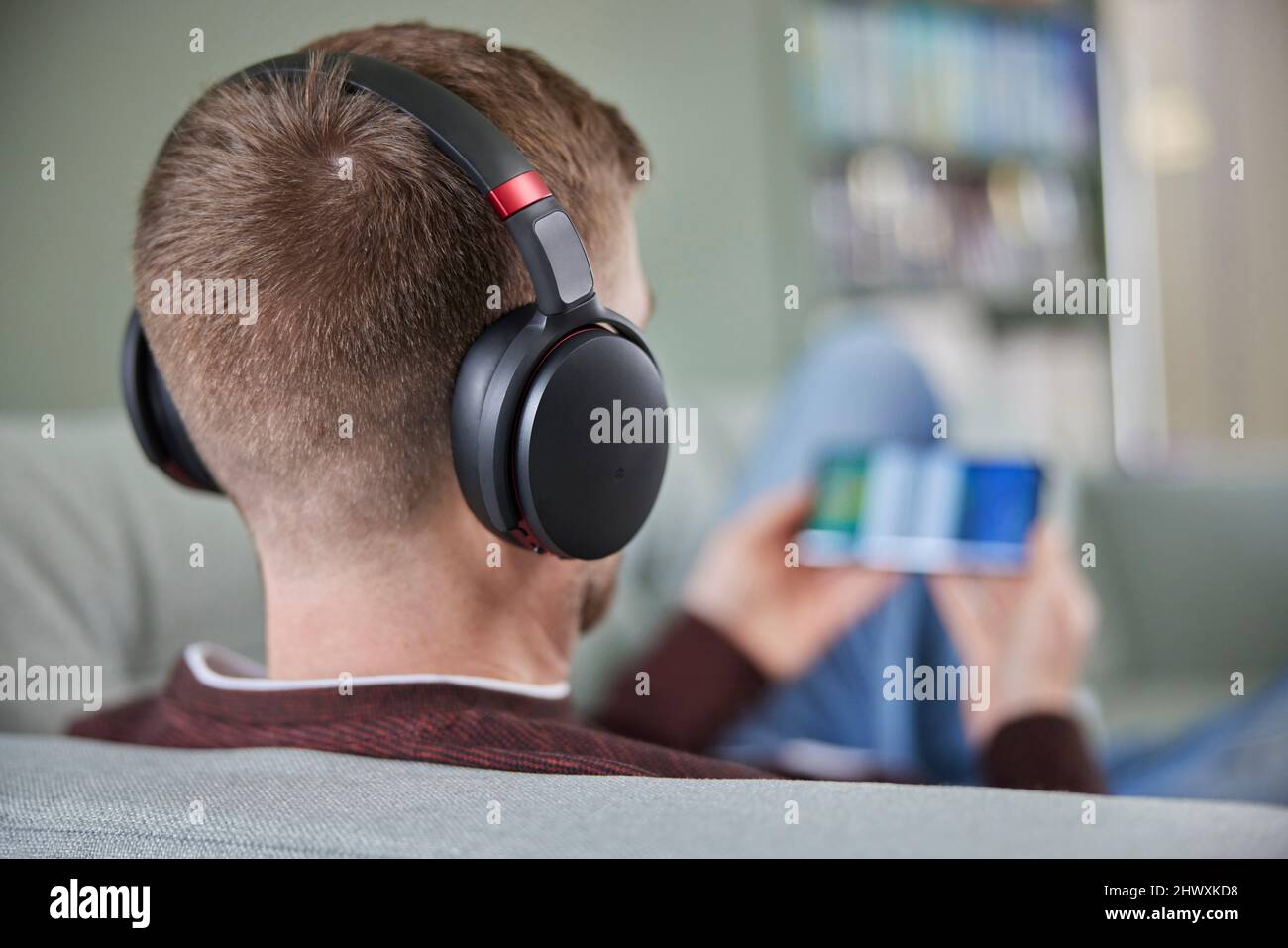 Rückansicht Des Mannes, Der Sich Auf Dem Sofa Entspannt, Mit Kabellosen Kopfhörern, Die Filmmusik Oder Podcast Vom Mobiltelefon Streamen Stockfoto