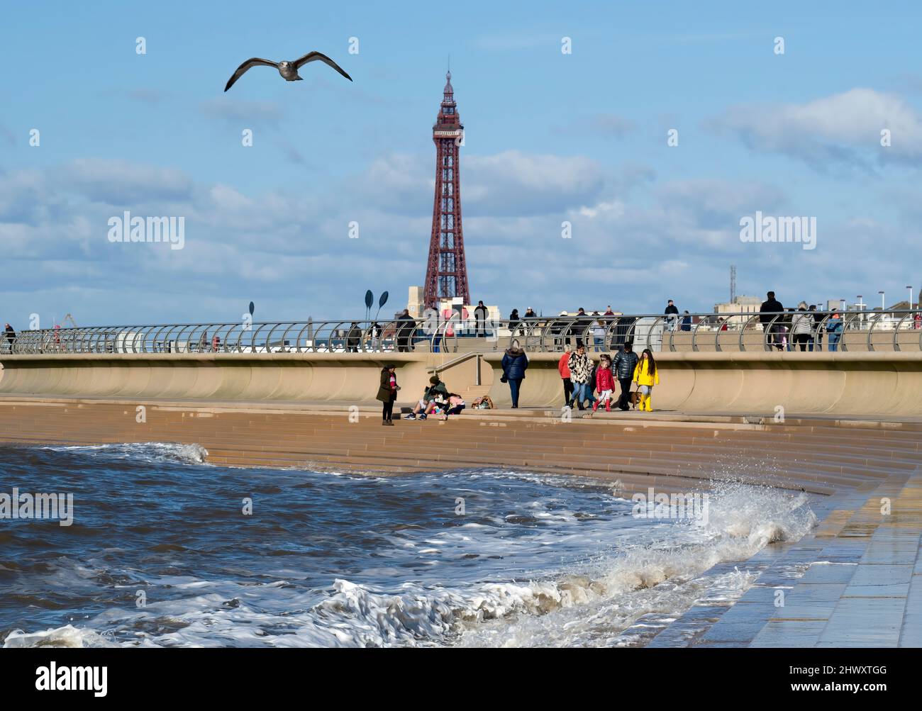 An einem hellen, sonnigen Tag treffen Urlauber auf den Sandstrand im Schatten des weltberühmten Blackpool Tower in Blackpool, Lancashire, Großbritannien Stockfoto