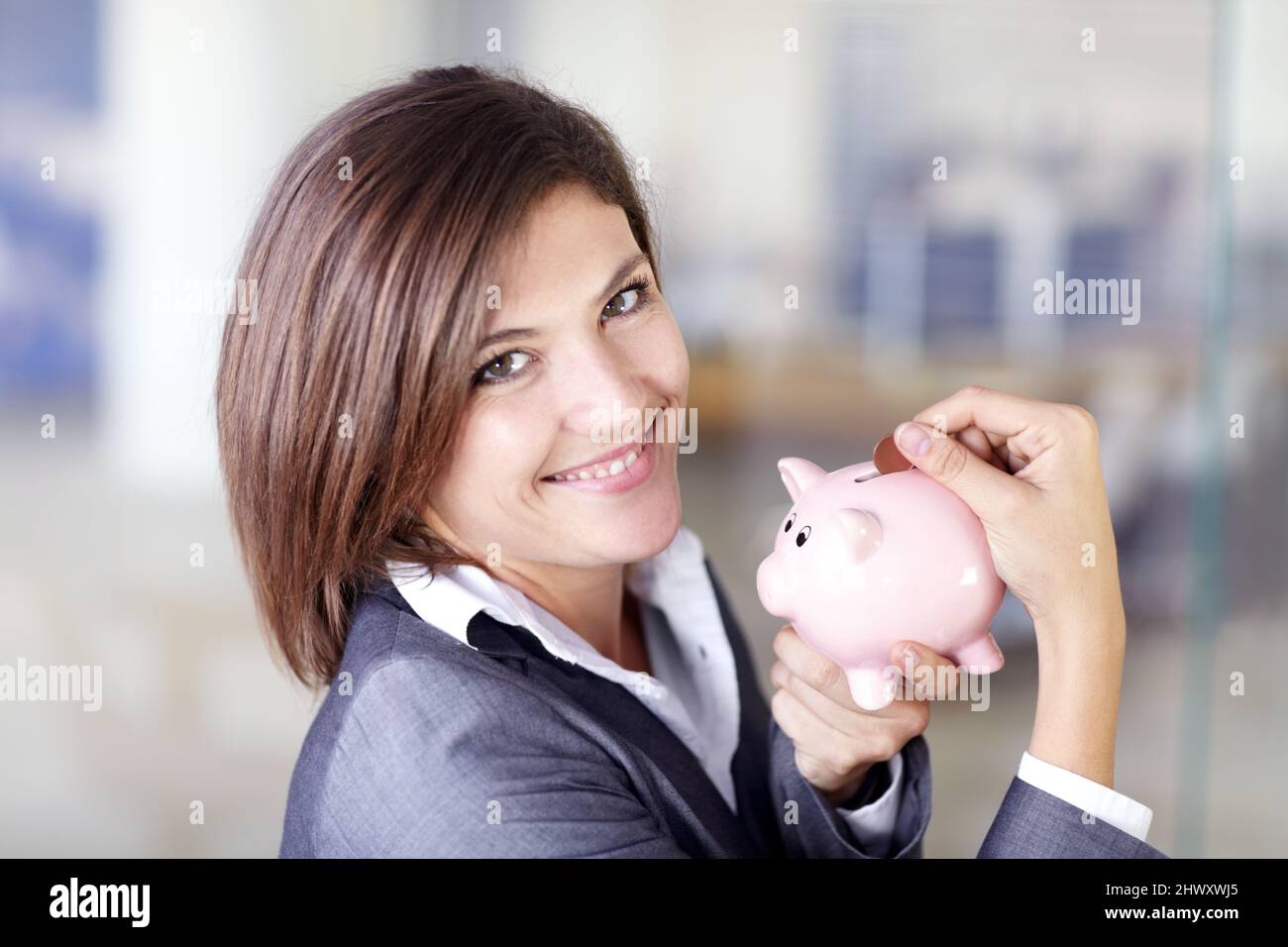 Jedes kleine bisschen zählt. Porträt einer attraktiven Geschäftsfrau, die eine Münze in ein Sparschwein legt. Stockfoto