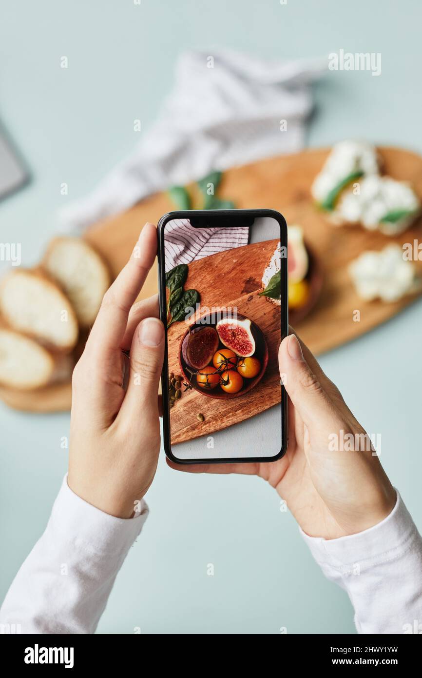 Minimale Draufsicht auf junge Frau, die mit dem Smartphone im Heimstudio ein ästhetisches Foto von Lebensmitteln fotografiert Stockfoto