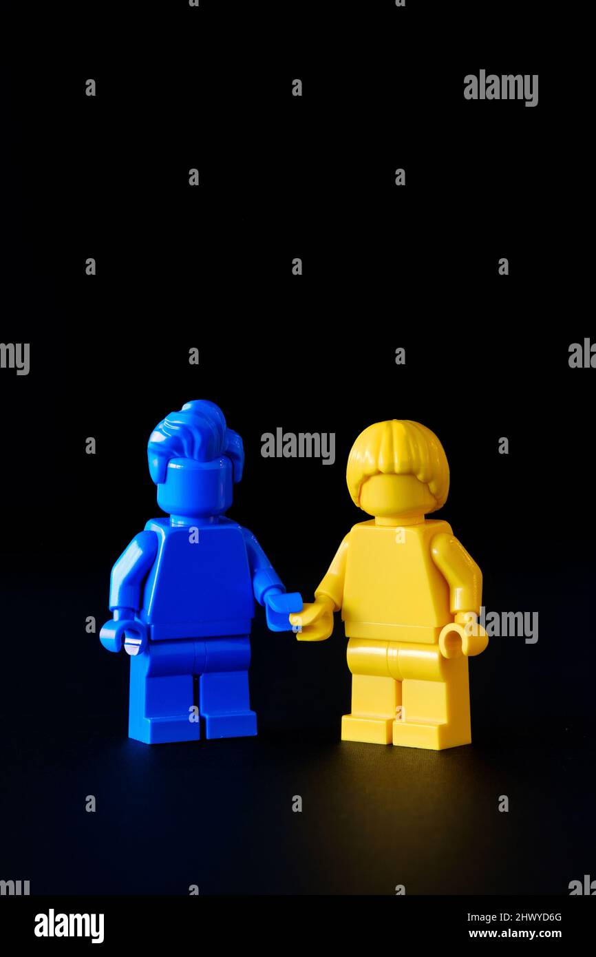 Zwei Lego-Zeichen, eine blaue und die andere gelbe, halten die Hände. Die Farben repräsentieren die ukrainische Flagge, um Solidarität während des aktuellen Krieges zu zeigen Stockfoto
