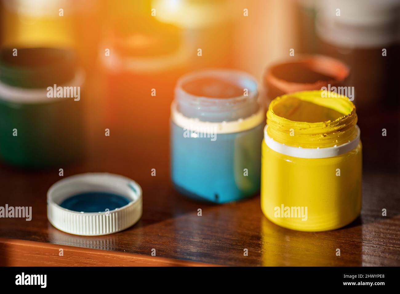 Auf dem Schreibtisch befinden sich Gläser mit farbenfroher Farbe zum Zeichnen. Helle Gouache- oder Aquarellfarbe. Hintergrund. Stockfoto