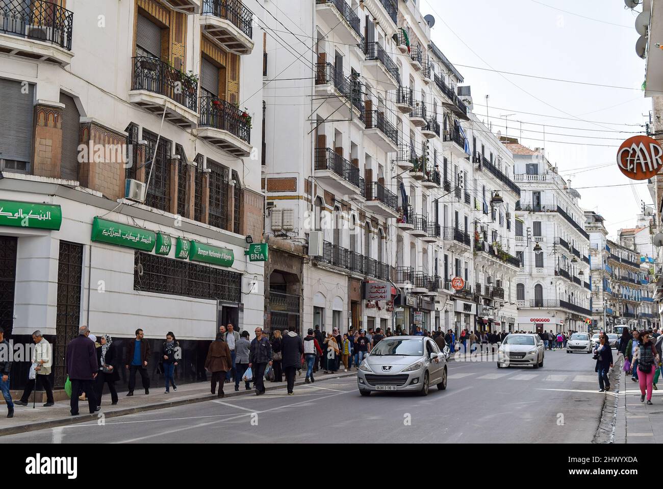 Menschenmenge, die auf der Didouche Mourad Straße in der Innenstadt von Algier zu Fuß unterwegs ist. Autos im Stau. Stockfoto