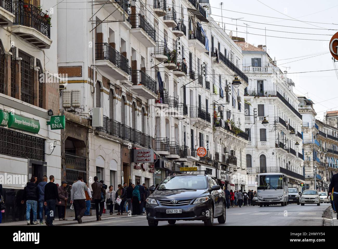 Menschenmenge, die auf der Didouche Mourad Straße in der Innenstadt von Algier zu Fuß unterwegs ist. Autos im Stau. Stockfoto