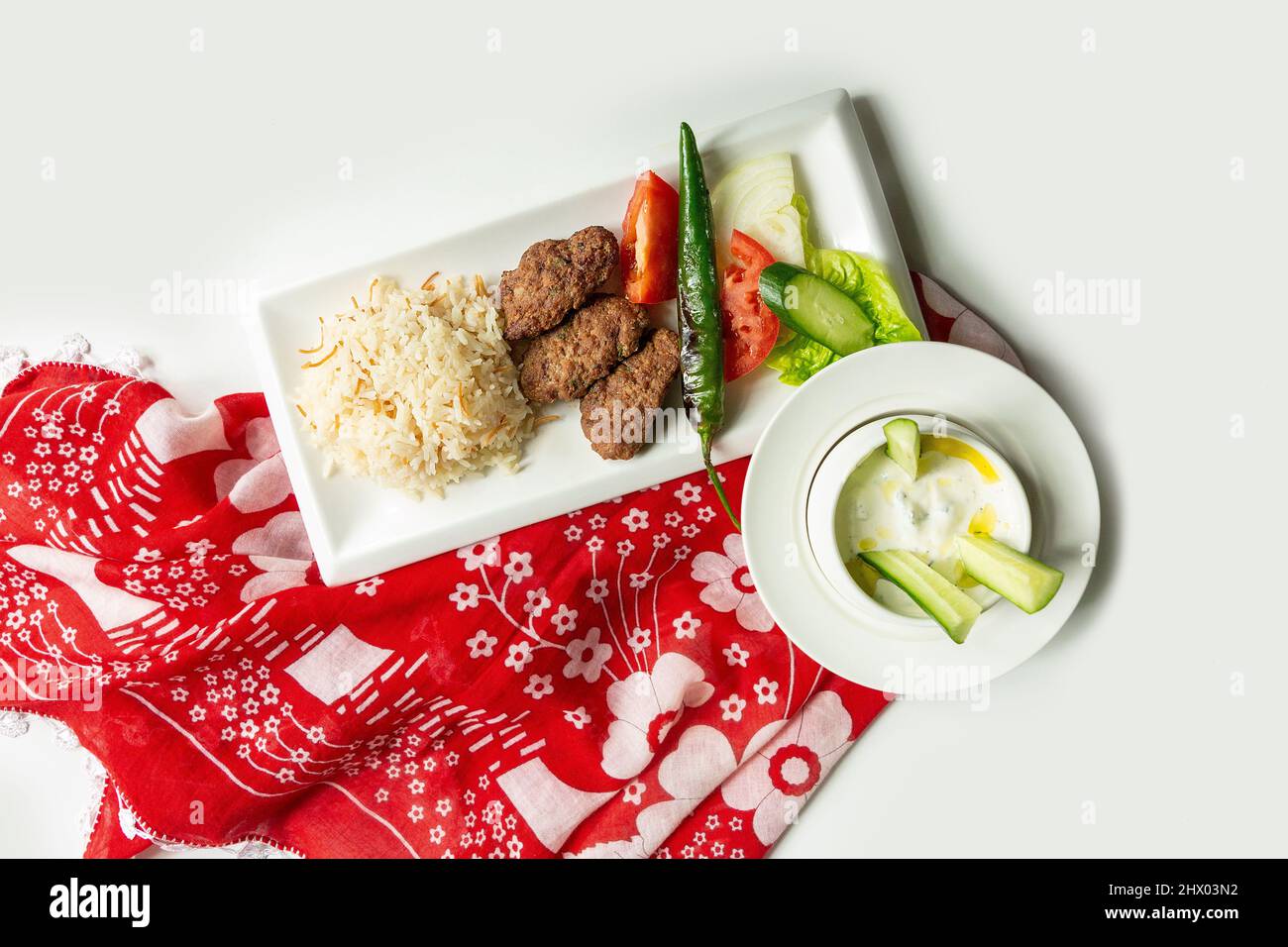 Traditionelle türkische Küche Izgara Kofte wuth Reis, Raita und Salat in einem Gericht isoliert auf bunten Tischtuch Draufsicht auf grauem Hintergrund Stockfoto