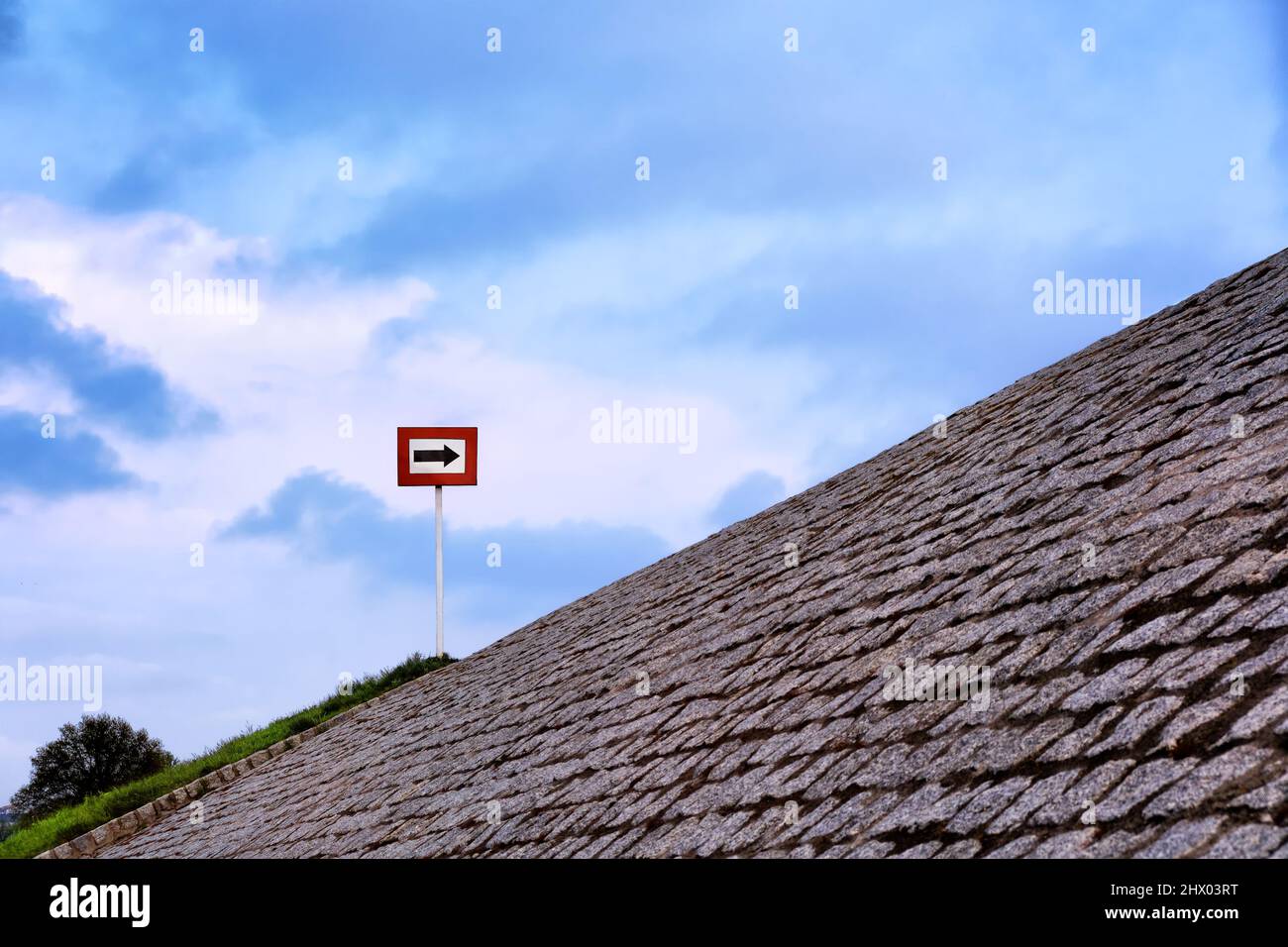 Schwarzer Pfeil auf weißem Hintergrund und in rotem Rahmen, der tagsüber auf einem gepflasterten Hügel steht. Blauer Himmel mit großen Wolken. Platz kopieren, Konzept Stockfoto
