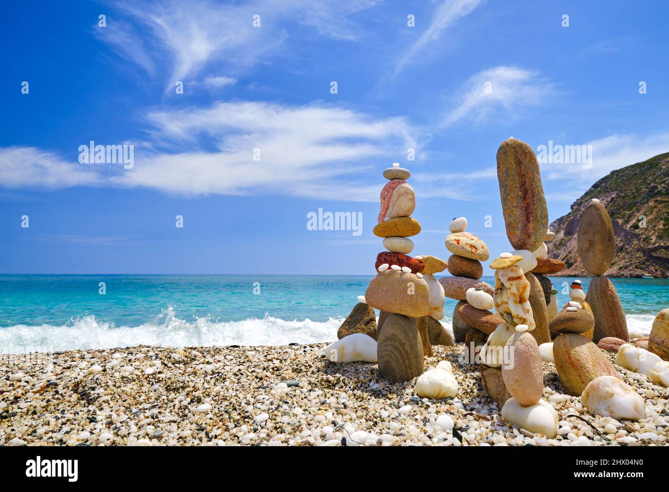 Gruppe von balancierenden Steinen am Strand. Heller, sonniger Tag, Sommerstimmung, azurblaues Wellenwasser am Kiesstrand, blauer Himmel und leichte Wolken Stockfoto