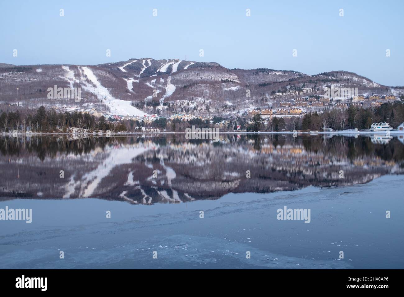 Mont-Tremblant Skipisten spiegeln sich in einem See, aufgenommen an einem teilweise sonnigen, nebligen Wintertag Stockfoto