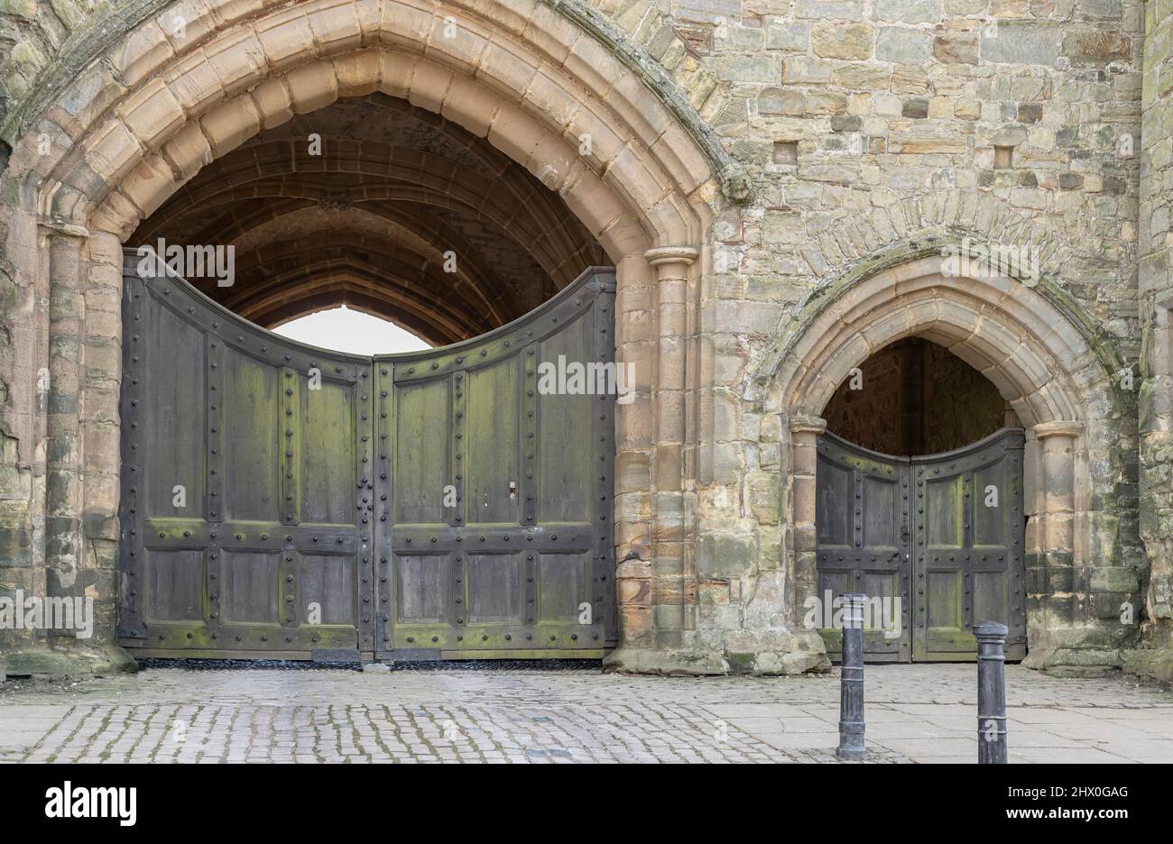 Eine große und kleine gewölbte Tür aus honigfarbenem Stein in einem Schloss mit einem schwarzen Tor auf jedem Torbogen mit Nieten Stockfoto