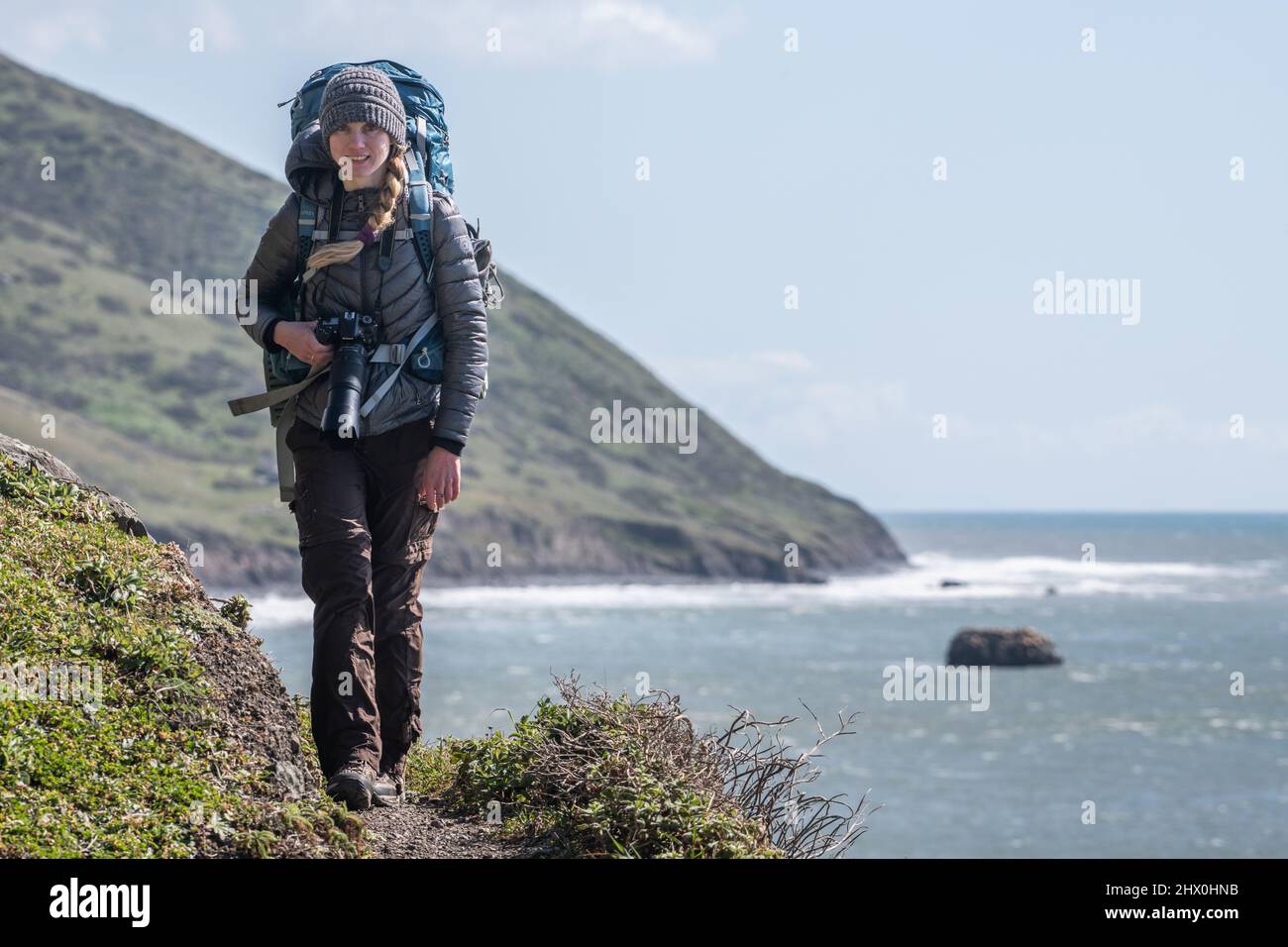 Eine blonde Backpacker-Frau, die mit ihrer Kamera und ihrem Rucksack auf dem verlorenen Küstenpfad im Humboldt County, Nordkalifornien, läuft. Stockfoto