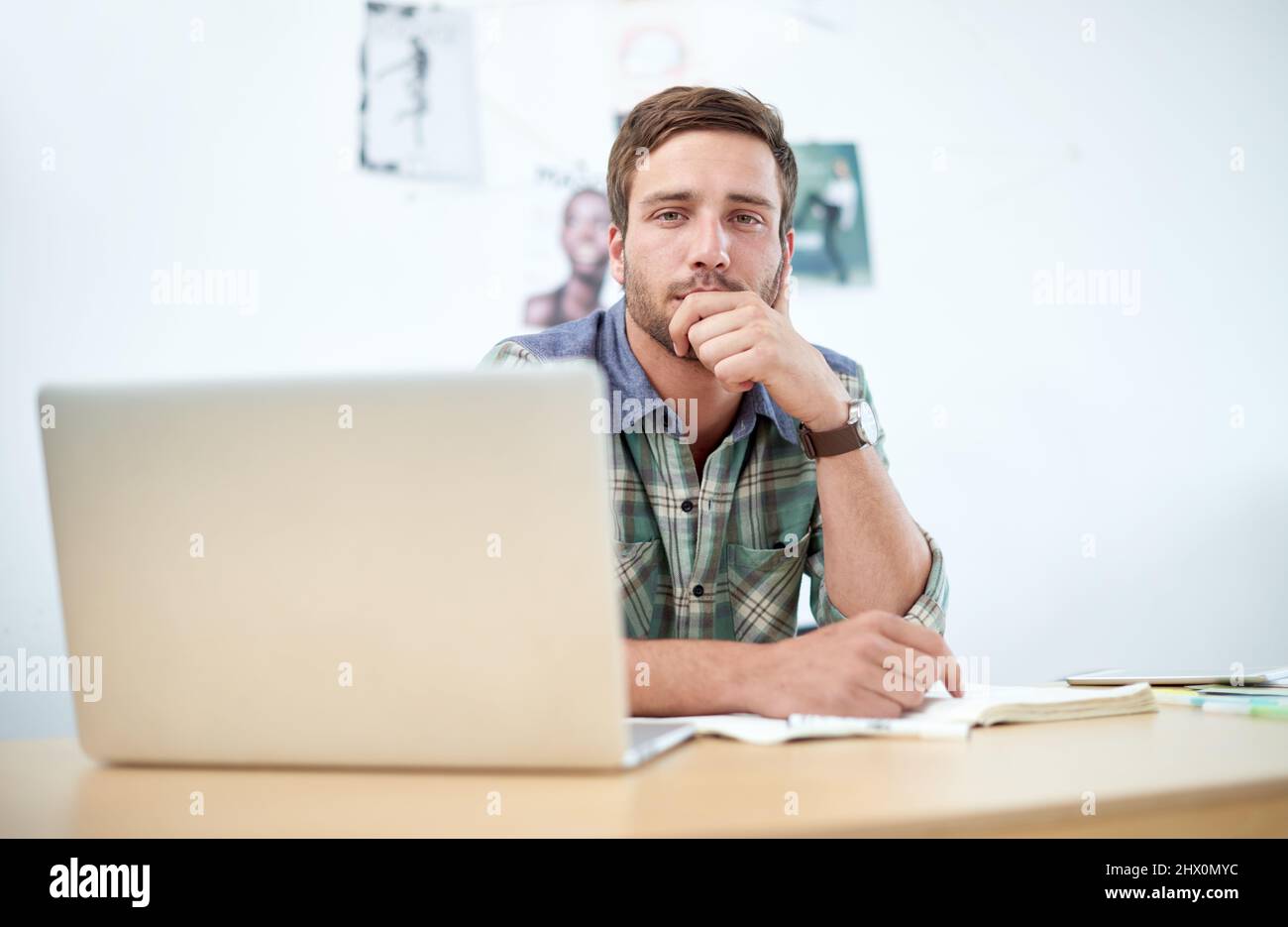 Porträt eines lässig gekleideten jungen Mannes, der ein digitales Tablet an seinem Schreibtisch verwendet. Die in diesem Bild gezeigten kommerziellen Designs stellen eine Simulation von dar Stockfoto
