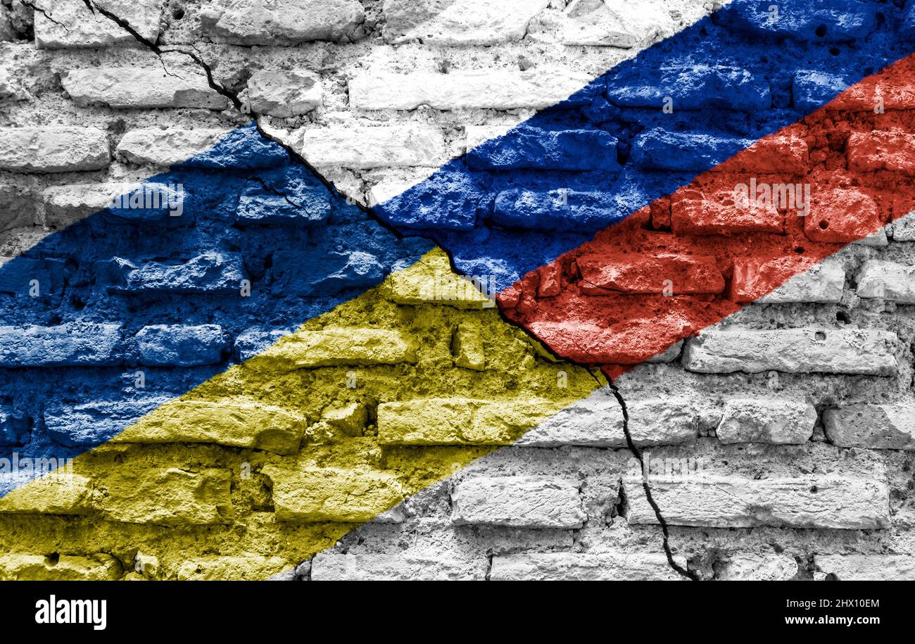 Die Flaggen der Ukraine und Russlands bemalten auf einer zerstörten gemauerten Mauer und wurden durch einen diagonalen Riss geteilt. Internationale diplomatische Beziehungen. Stockfoto