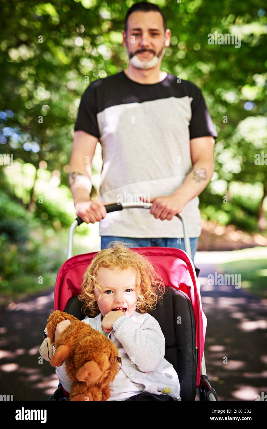 Spaziergang durch den Park. Porträt eines Vaters, der seine kleine Tochter in einen Kinderwagen nach draußen schiebt. Stockfoto