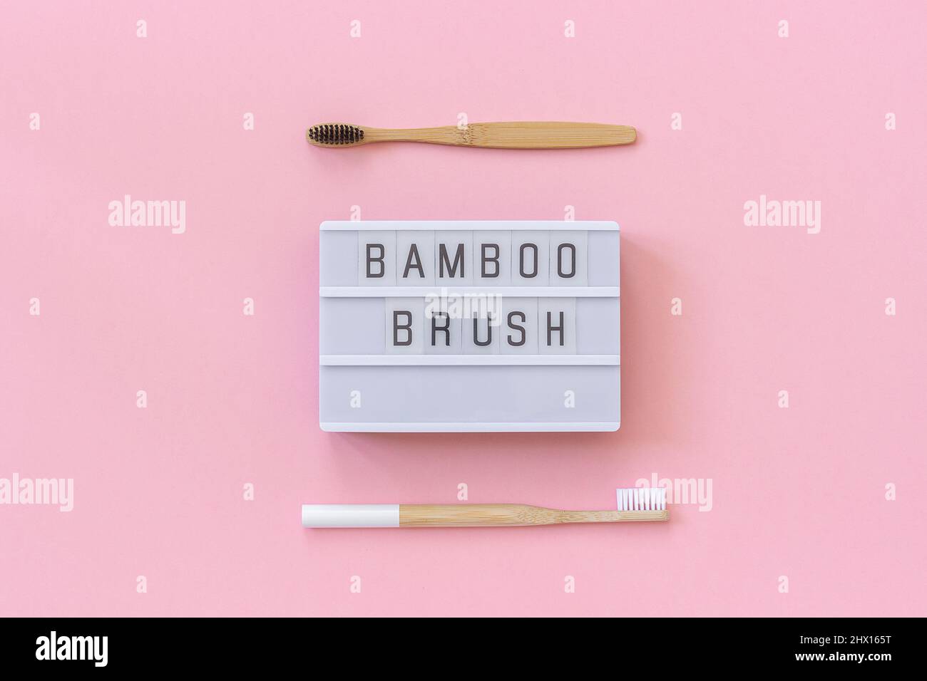 Zwei natürliche, umweltfreundliche Bambusbürsten mit weißen und schwarzen Borsten und Lightbox-Text Bambus-Pinsel auf papierrosafarbenem Hintergrund. Draufsicht Flat Lay Templ Stockfoto