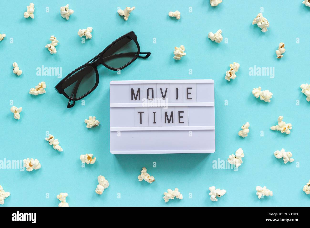 3D Gläser, Popcorn und Lightbox Text Movie Time auf blauem Papierhintergrund. Draufsicht Template Konzept Kino Film und Unterhaltung. Stockfoto
