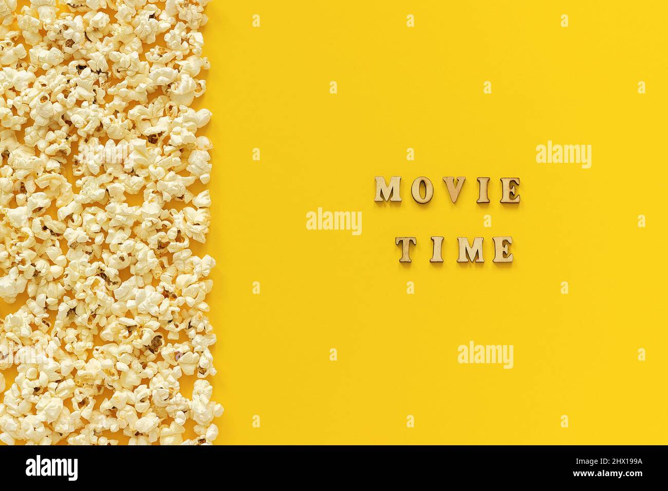 Verstreutes Popcorn am linken Rand und Filmzeit auf gelbem Papierhintergrund. Draufsicht Kopierbereich Vorlage für Text oder Ihr Design. Stockfoto