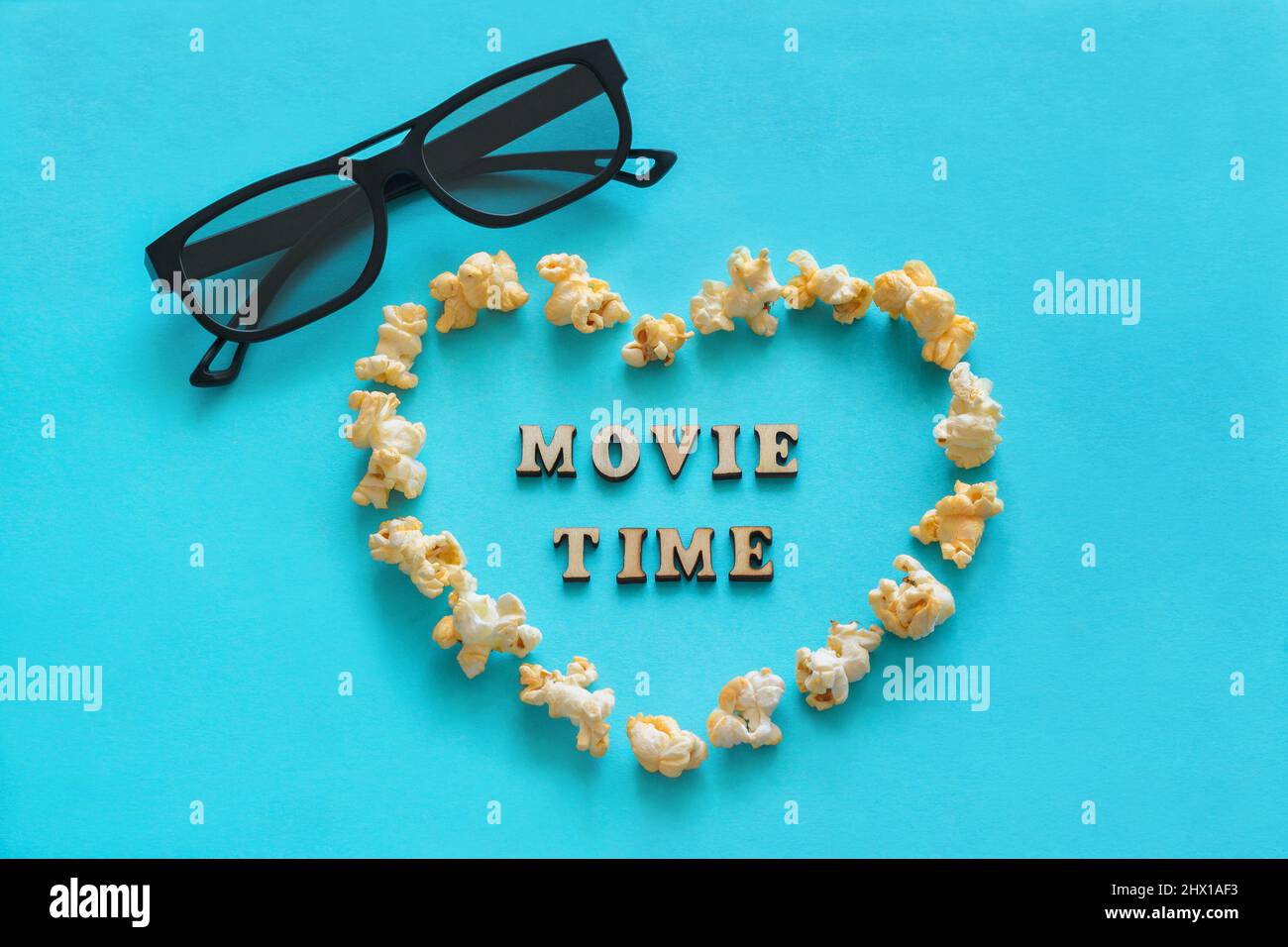 Popcorn in Form Herz, 3D Gläser, der Text 'Movie Time'. Stillleben auf blauem Hintergrund. Flach liegend, Draufsicht. Konzept - Liebe zum Kino, Liebhaber von Cine Stockfoto