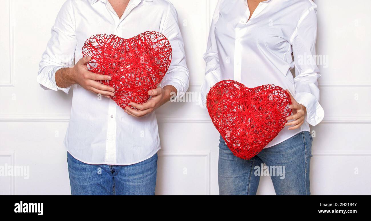 Mann und Frau in einem weißen Hemd und einer blauen Jeans mit roten Korbherzen. Romantische Fotosession im Studio am Valentinstag. Stockfoto