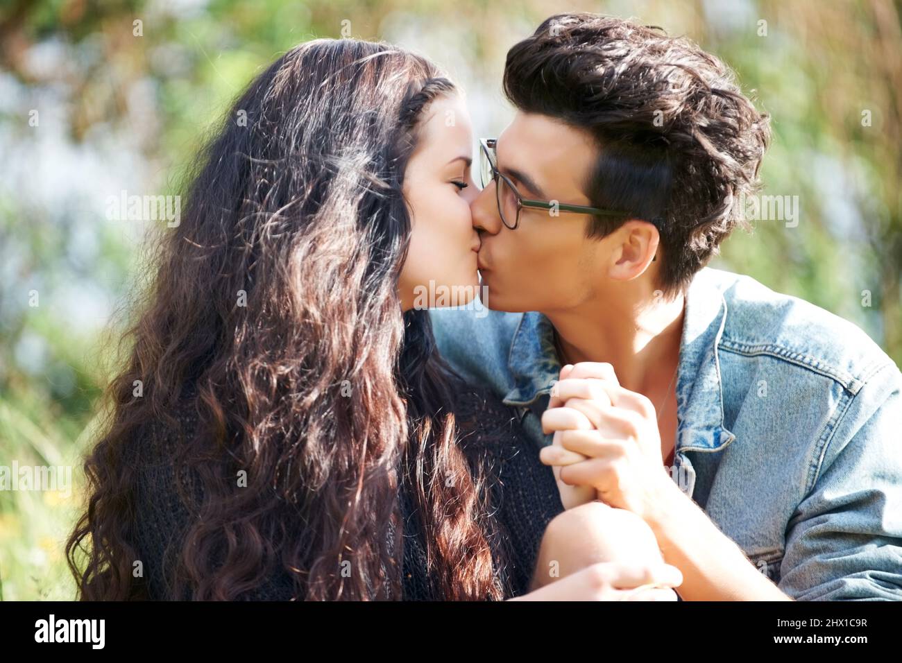 Einen intimen Kuss teilen. Nettes junges Paar, das draußen sitzt und einen romantischen Kuss teilt. Stockfoto