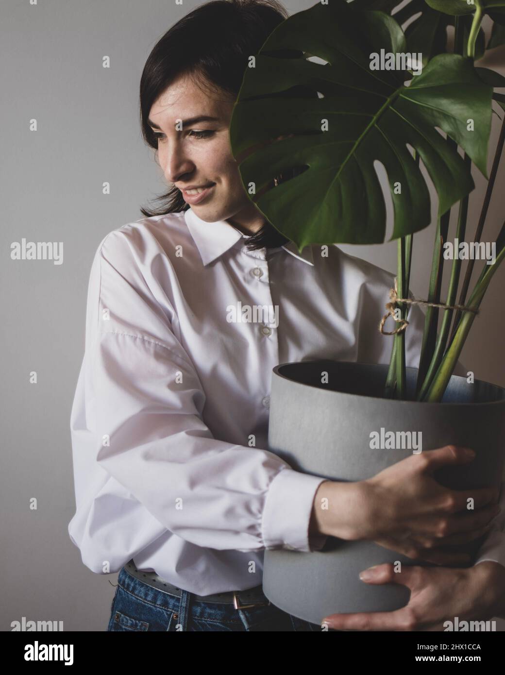 Die junge Frau steht mit einem großen Blumentopf mit Monstera Stockfoto