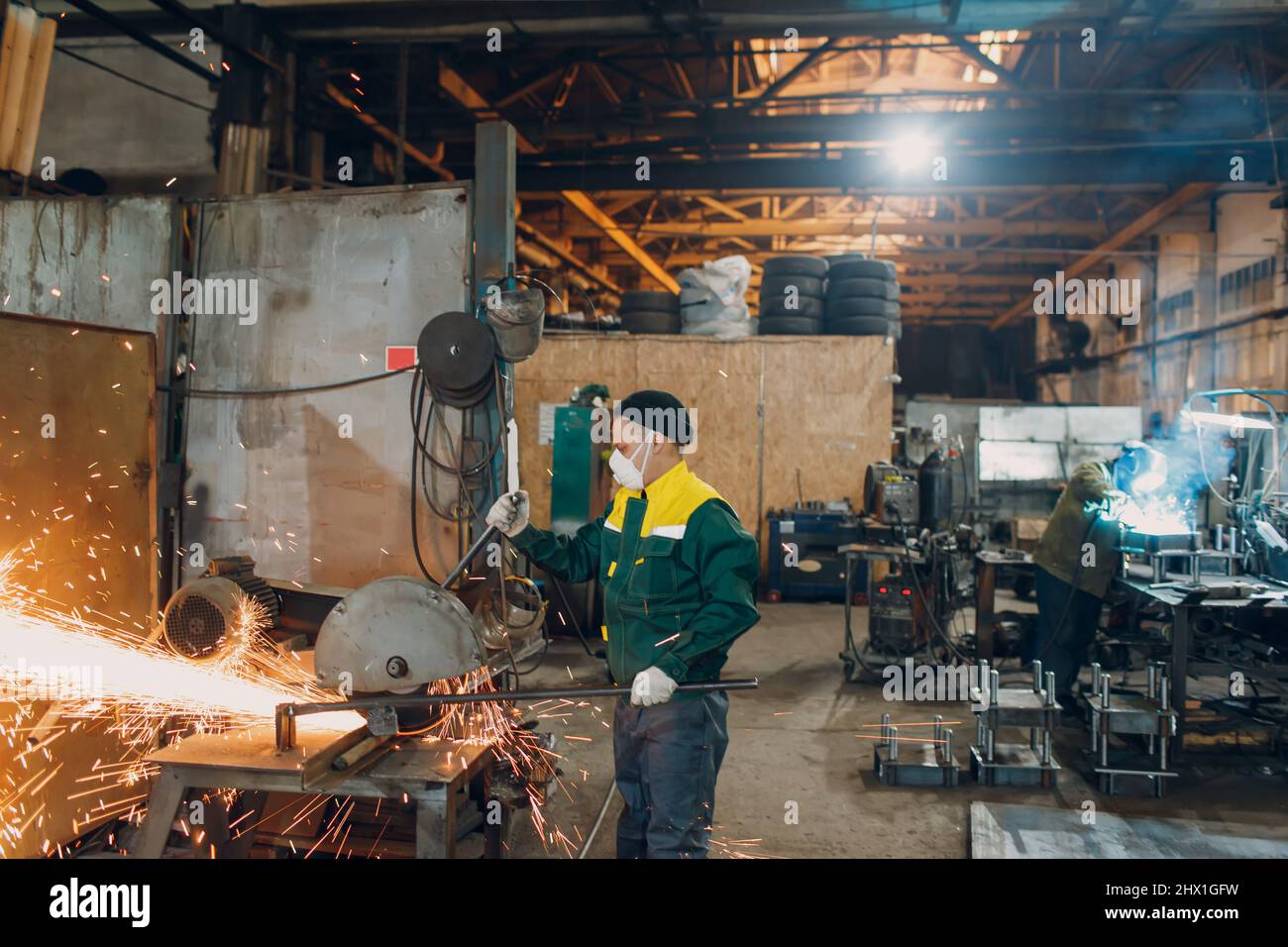 Arbeiter, die im Werk mit Metallkonstruktionen arbeiten. Metallbearbeitung mit großem Winkelschleifer, Scheibensäge und Schweißerschweißen. Funken in der Metallbearbeitung im Werk. Stockfoto