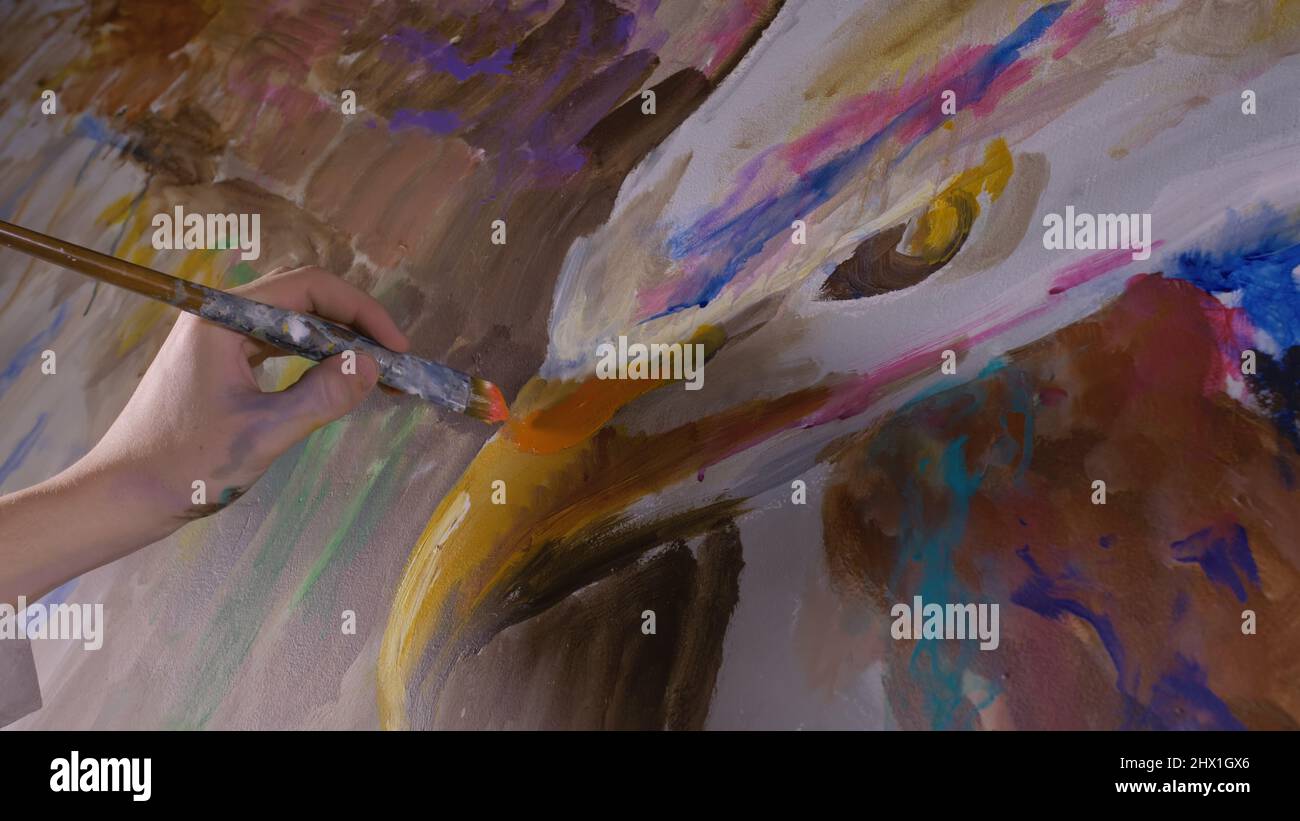 Der Designer zeichnet einen Adler an die Wand. Handwerker Dekorator malt ein Bild mit Acrylöl Farbe. Nahaufnahme mit dunklem magischem Kinosound. Maler Maler in einem Farbmantel gekleidet. Innen. Stockfoto