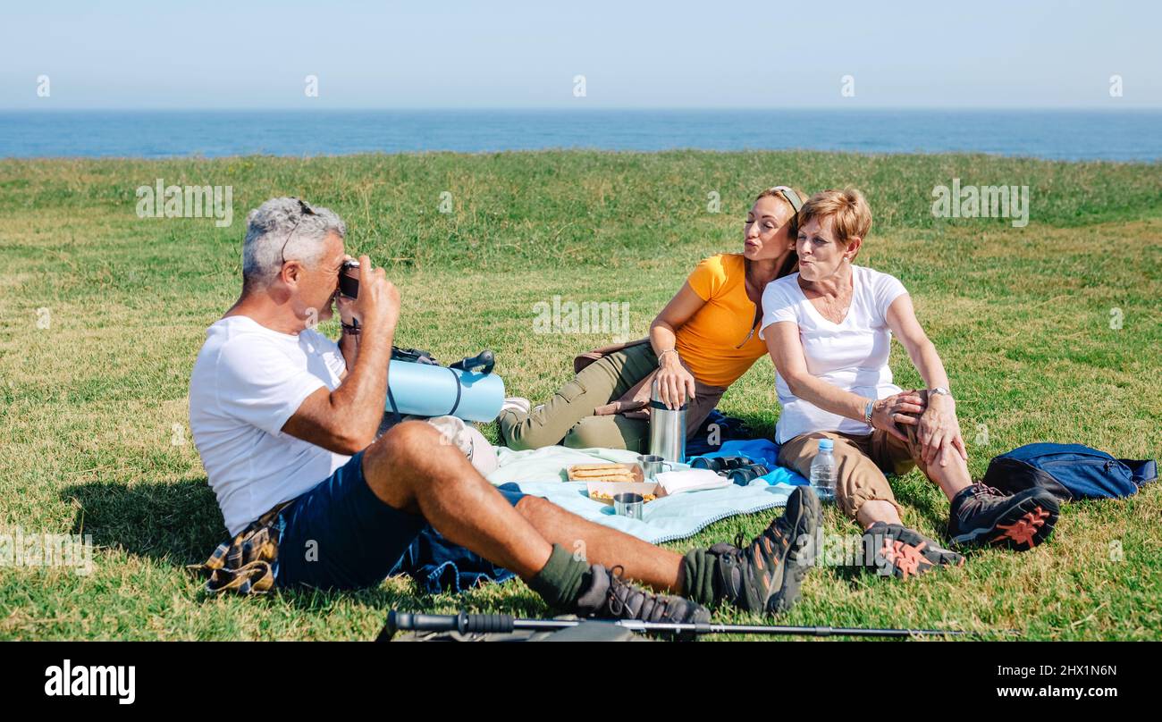 Älterer Vater, der seiner Familie ein Foto mit Entengesicht machte, das auf einer Decke saß und ein Picknick machte Stockfoto